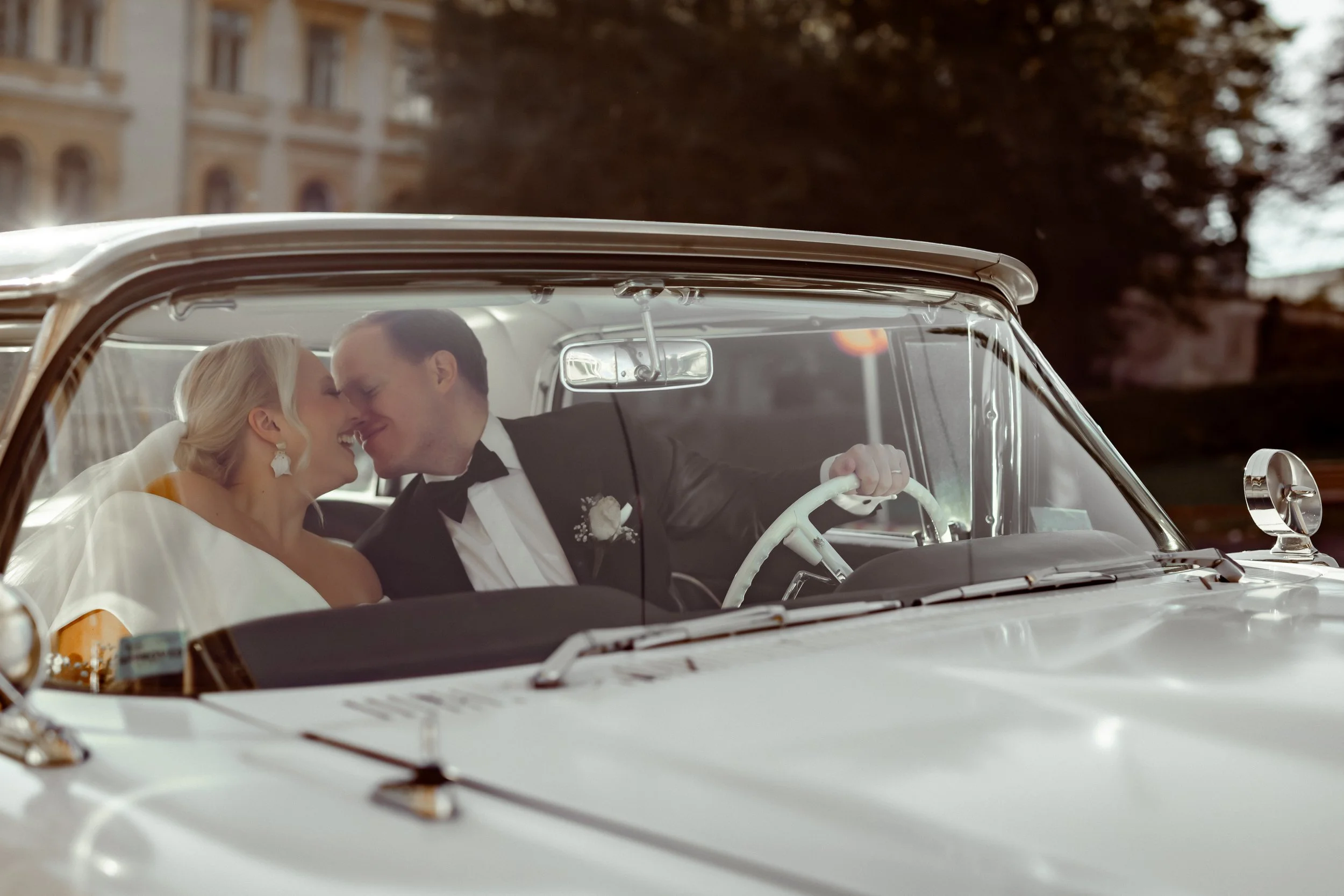 Hääpari istuu autossa, ja he suutelevat toisiaan, onnellinen hetki.