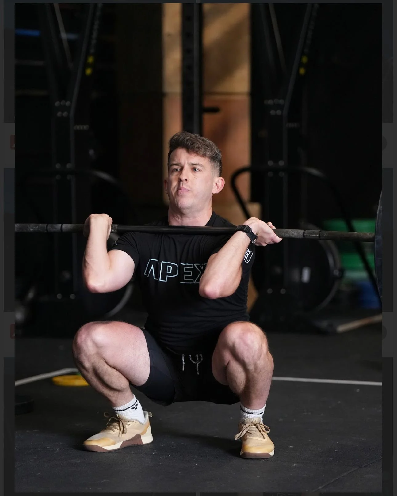 A man in black workout clothes squats while holding a barbell across his shoulders in a gym.