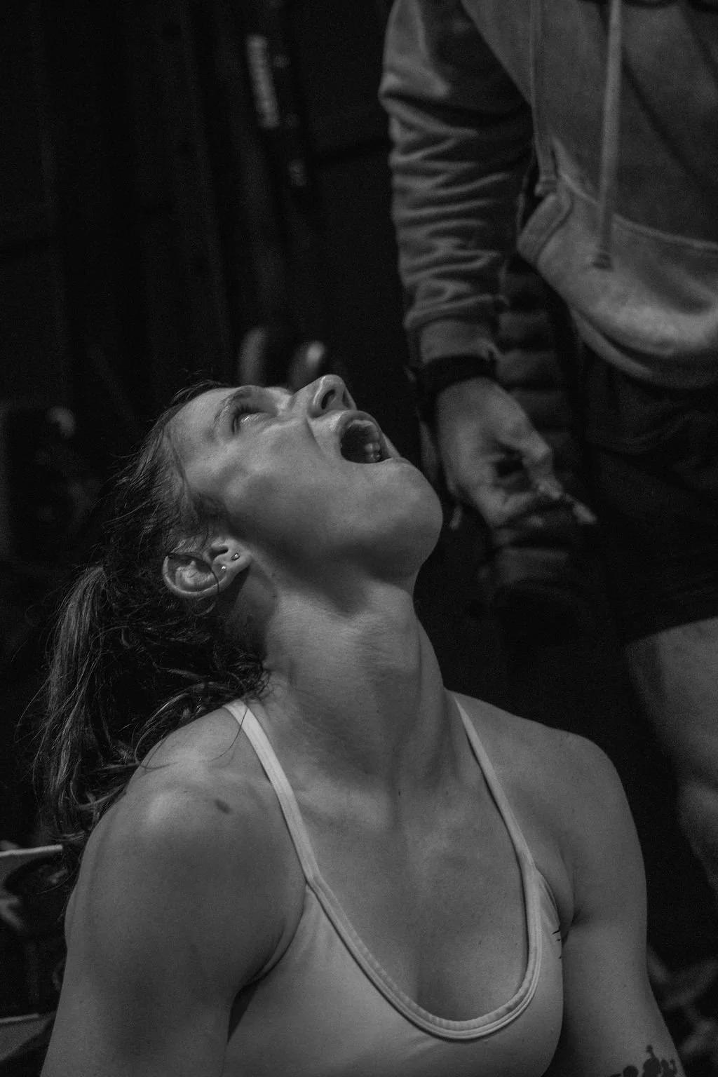 A woman with a tank top looking up with her mouth open, leaning back, in a dimly lit environment, possibly a bar or club.