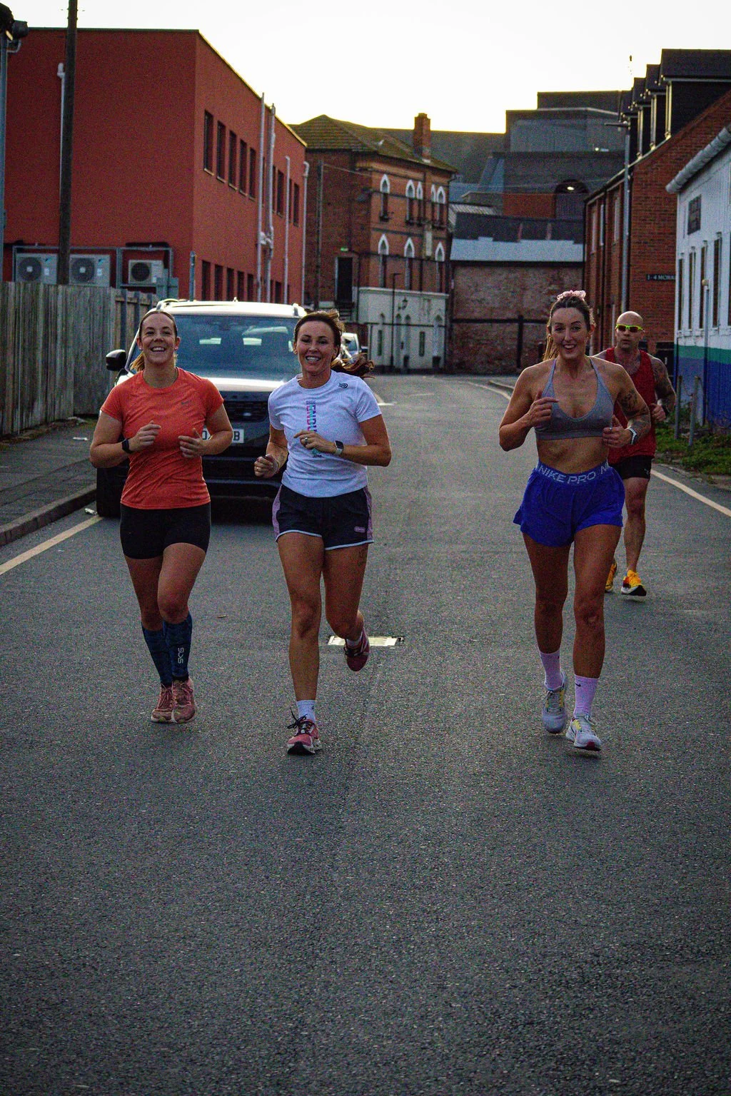Four women running together on a city street during dawn or dusk.