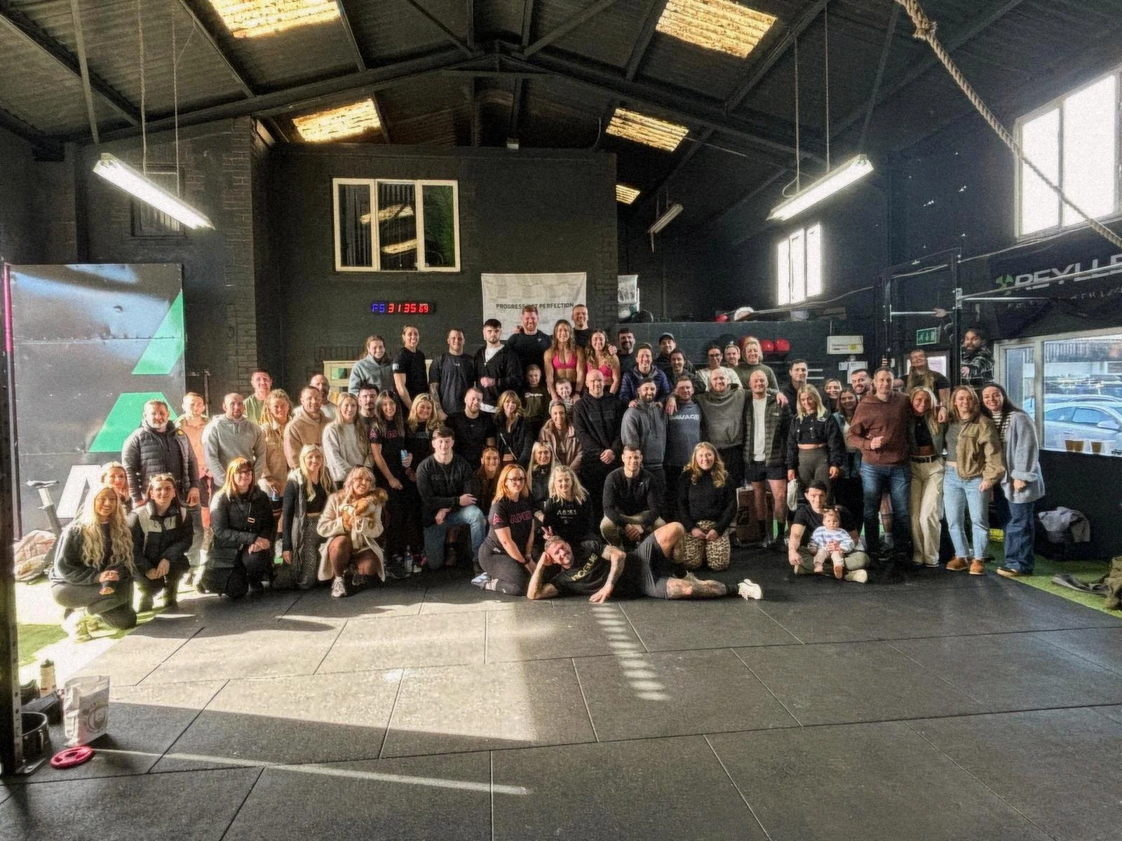 Large group of people gathered together in a gym, posing for a photo. The gym has a high ceiling, exposed beams, and gym equipment in the background.