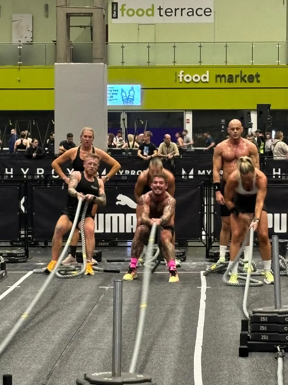 Group of muscular people participating in a crossfit competition in a gym, pulling weighted ropes.
