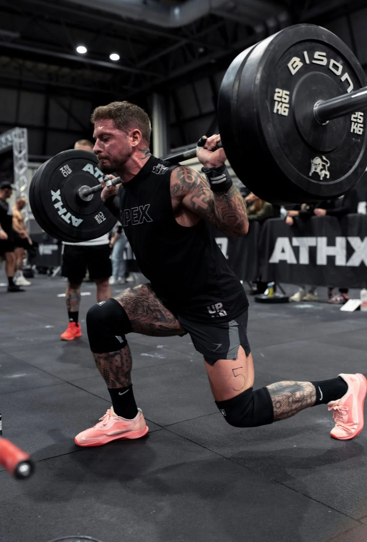 A man with tattoos demonstrates a weighted squat at a gym.