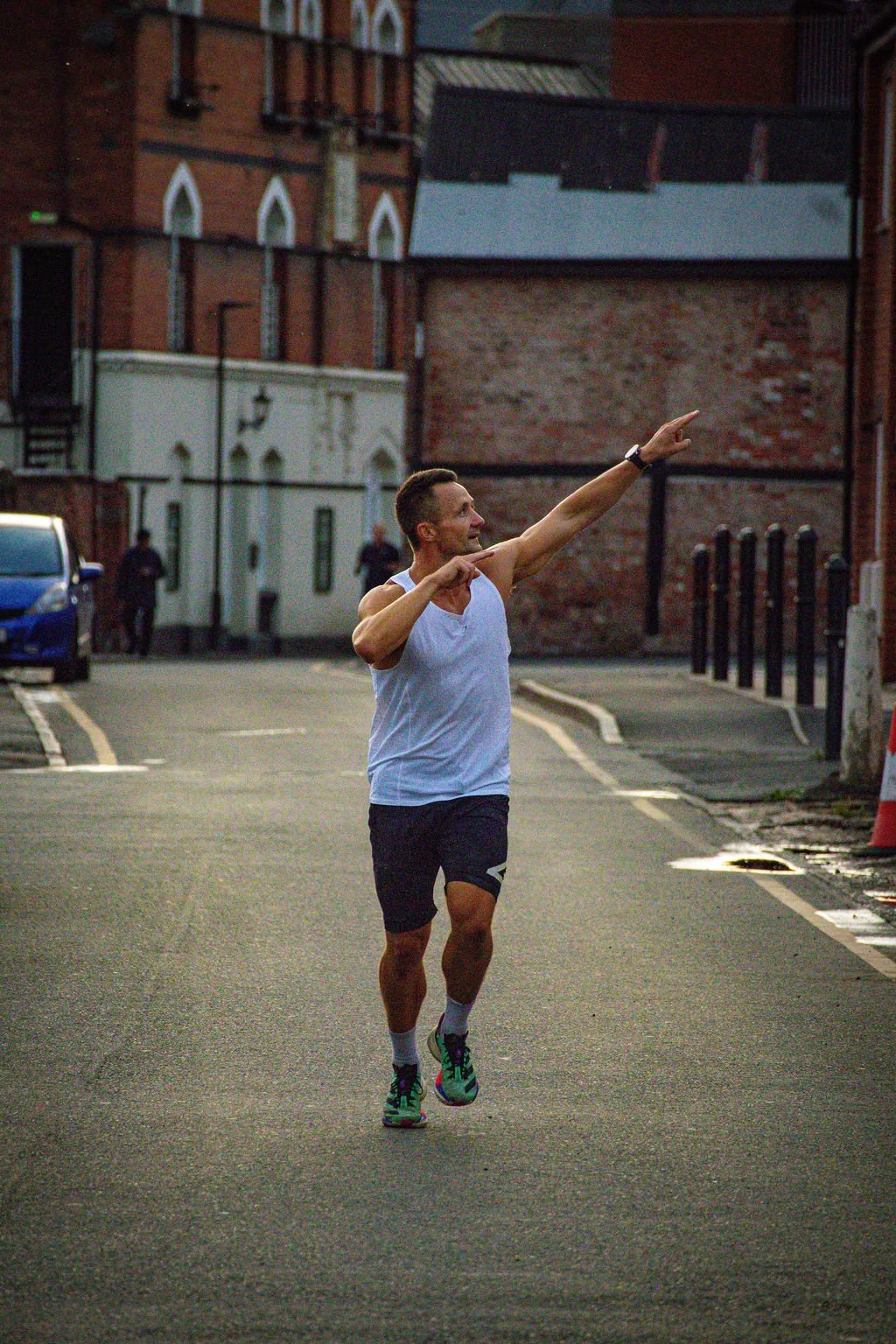 A man running on a street pointing with his left hand while jogging during dusk or dawn.