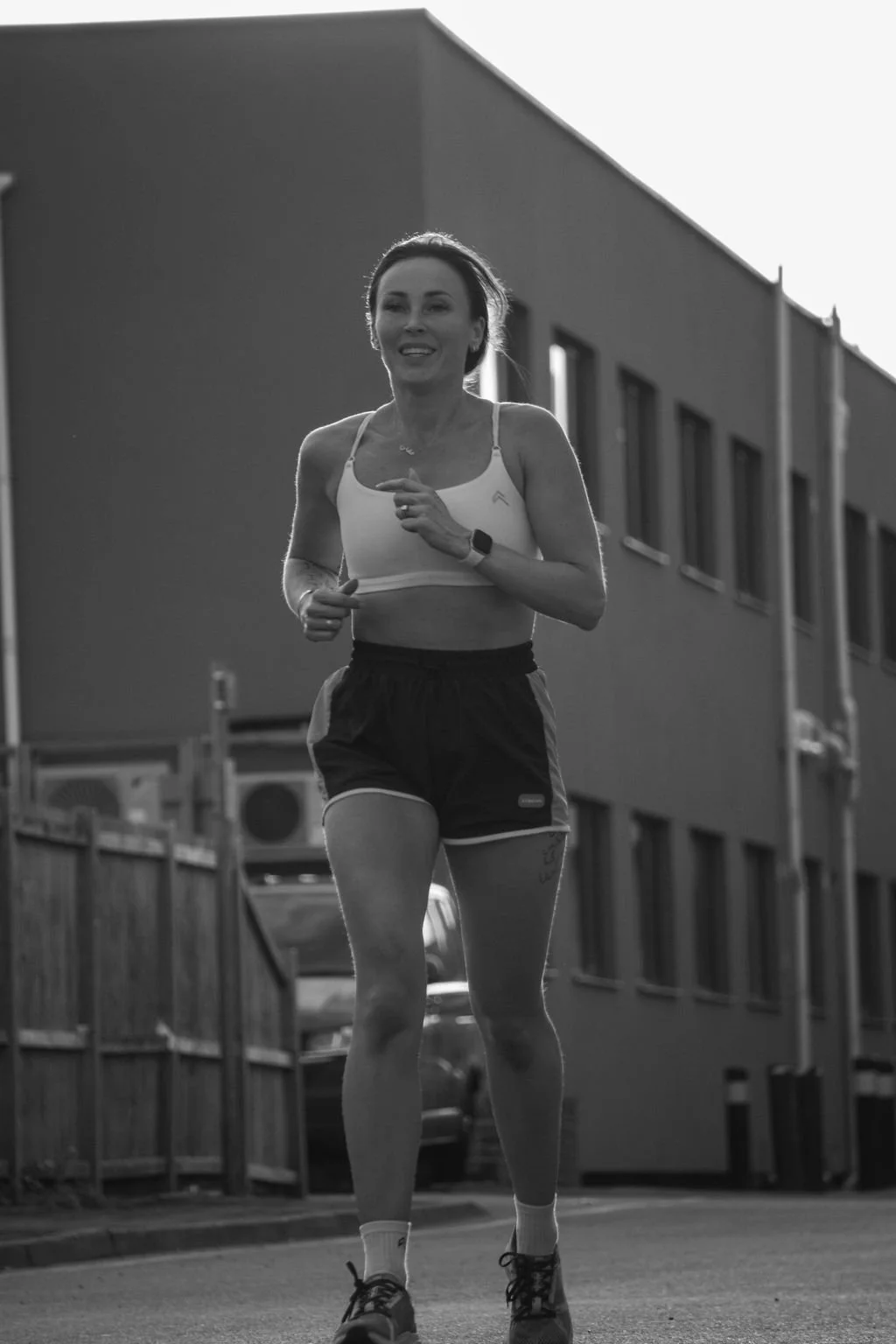 A woman jogging outdoors on a city street during daytime, wearing athletic clothing and a smartwatch.