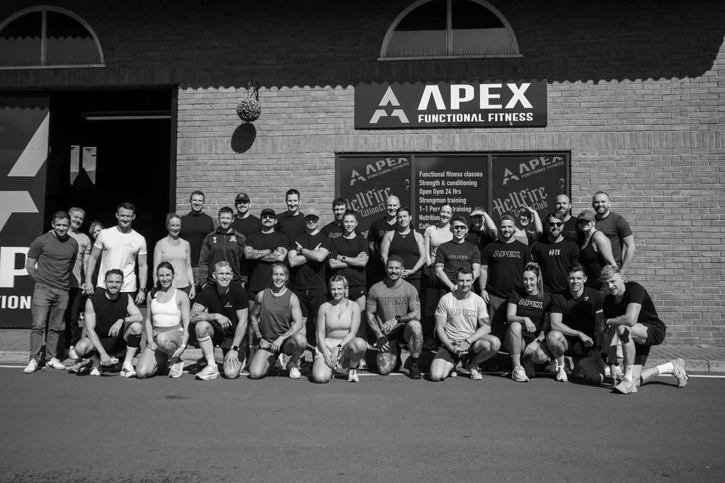 Group of people in athletic attire posing outside a fitness center called Apex Functional Fitness.