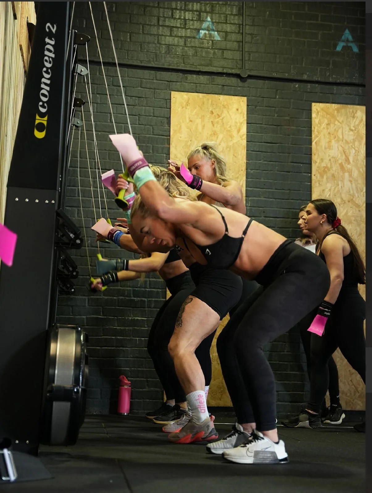 Member participating in a group workout session at a gym, bending over and using resistance bands attached to a wall.