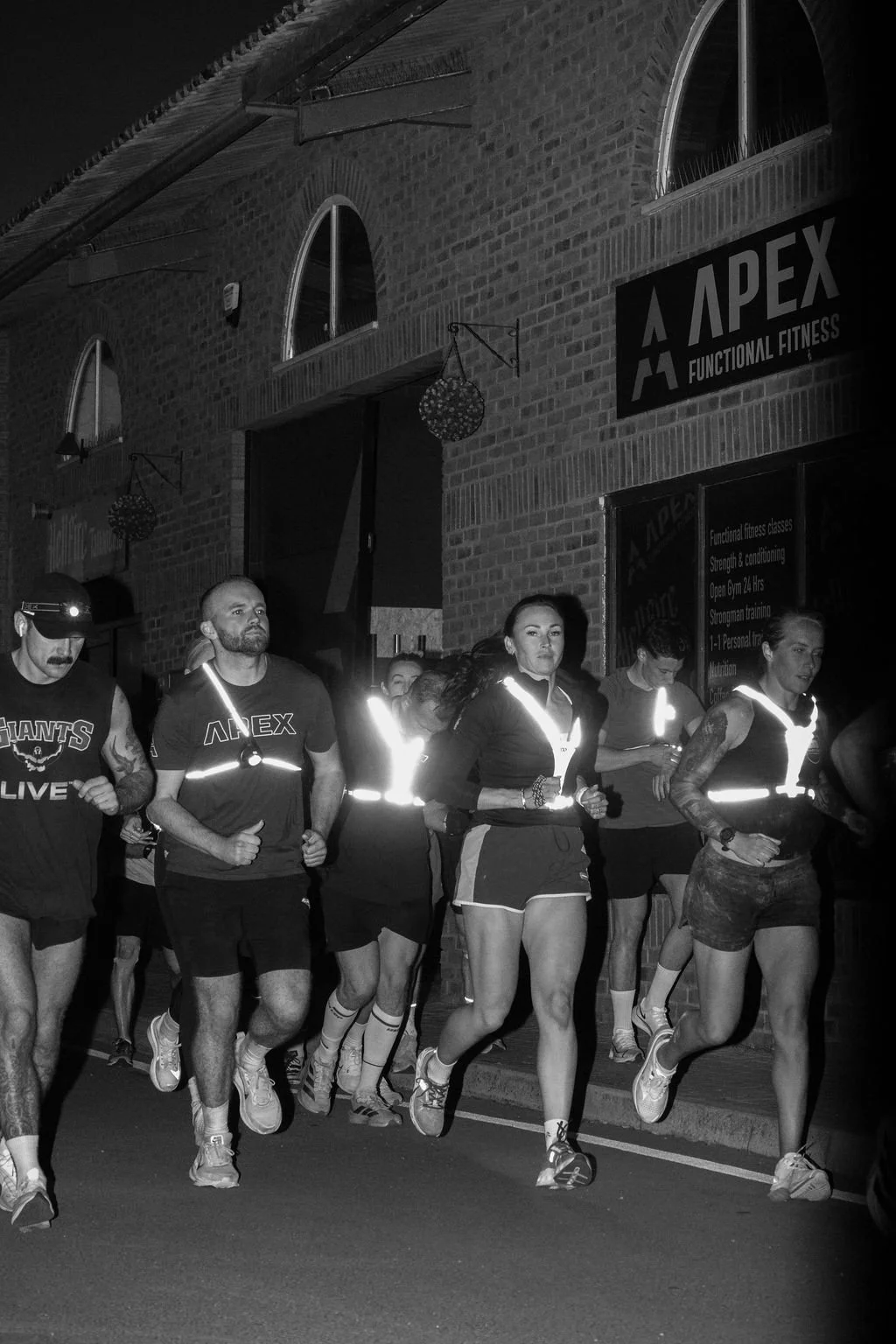 Group of people running at night in front of a gym with a sign that reads 'Apex Functional Fitness'
