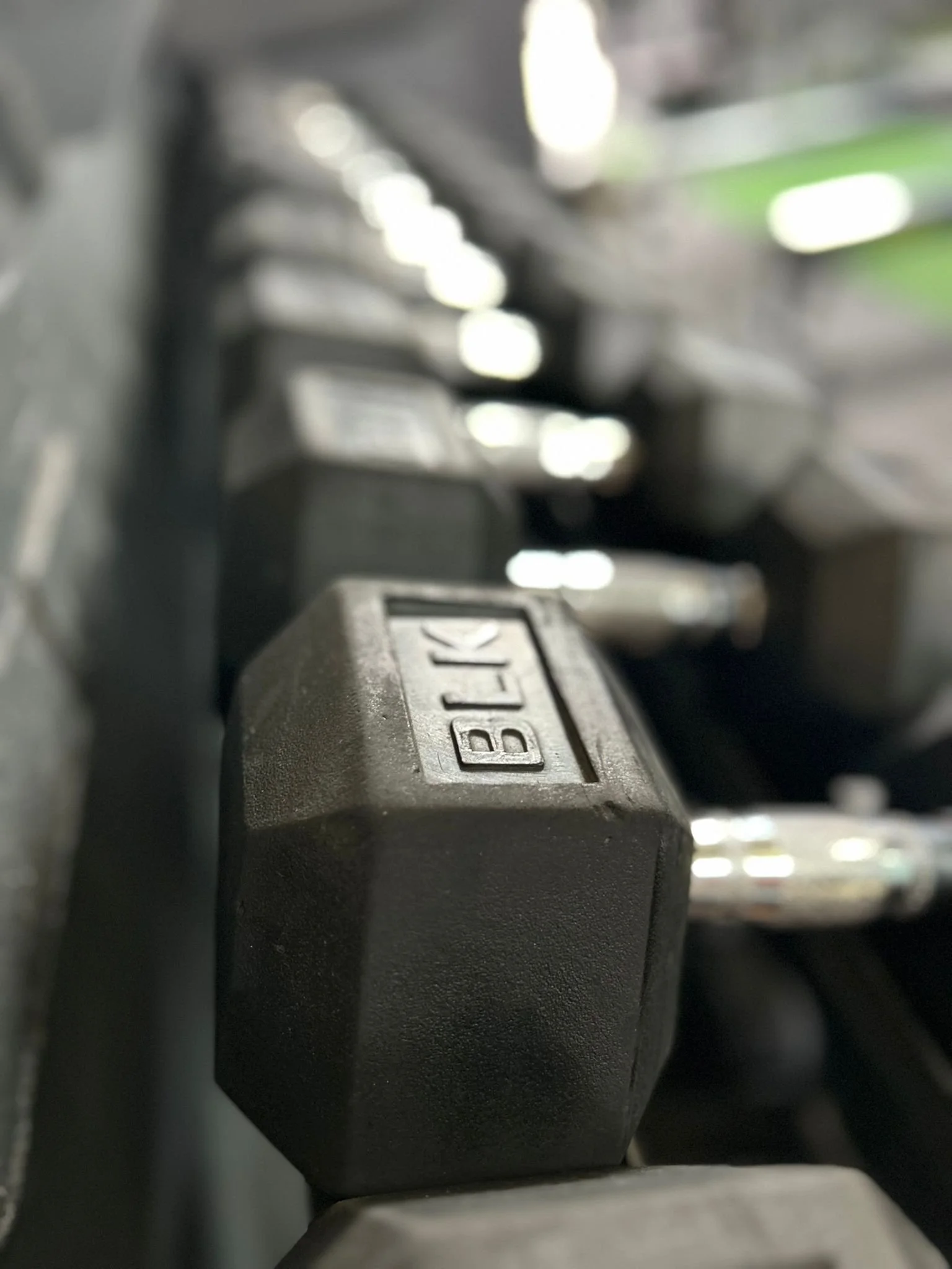 Close-up of a black dumbbell with the word 'BLACK' embossed on it, placed next to other similar dumbbells on a gym rack.