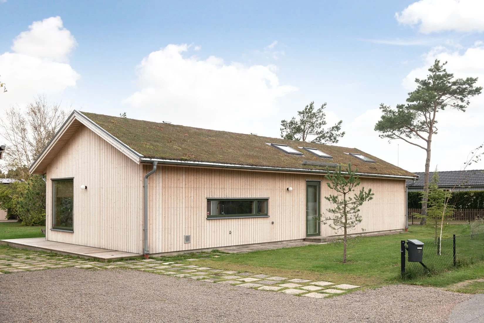 En modern enplanshus med träfasad och stora fönster, omgivet av gräs och små träd.