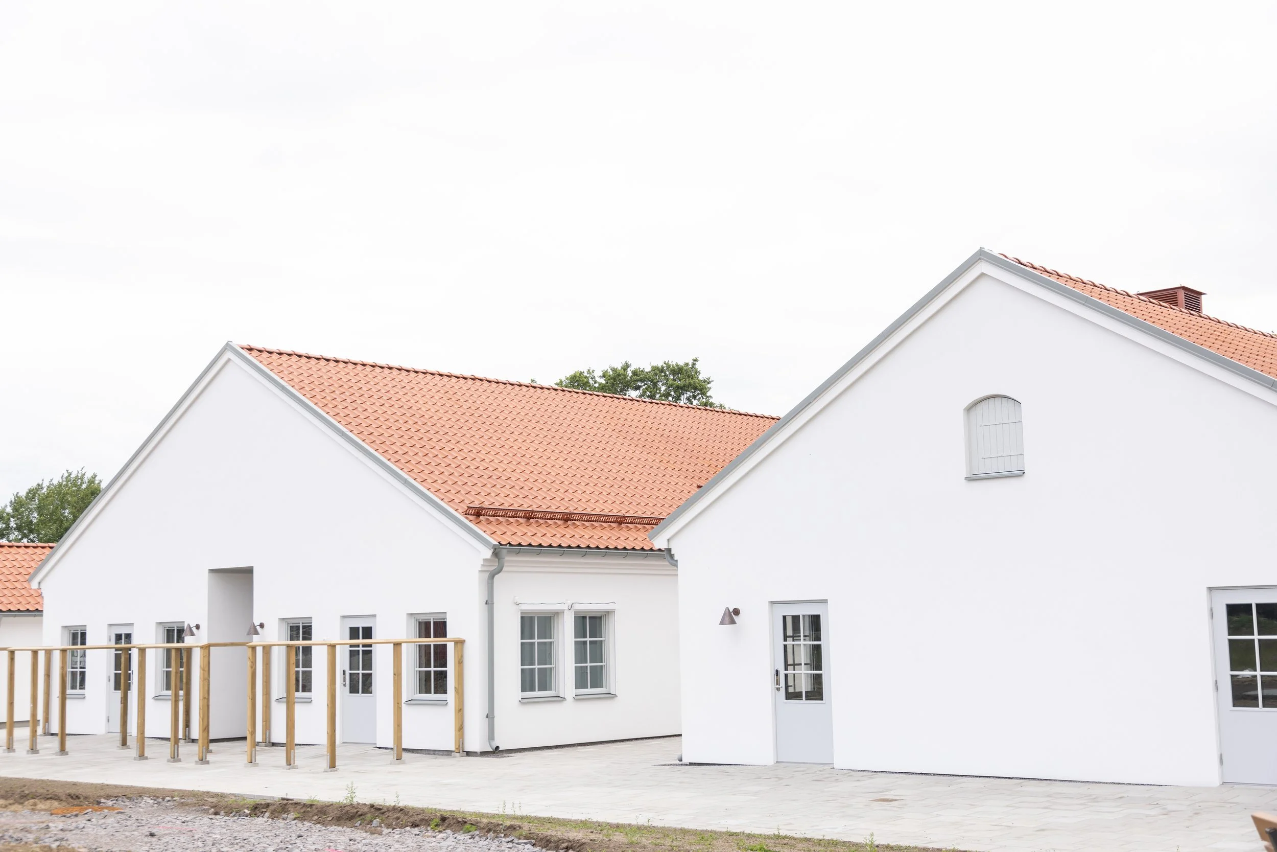 Vit villa med röda tegeltak, vitmålad fasad, flera fönster och dörrar, nybyggd med trädäck och omgärdande trädgård.