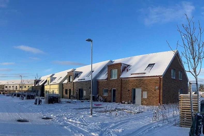 Fler nybyggda hus med snötäckta tak i ett vinterlandskap.