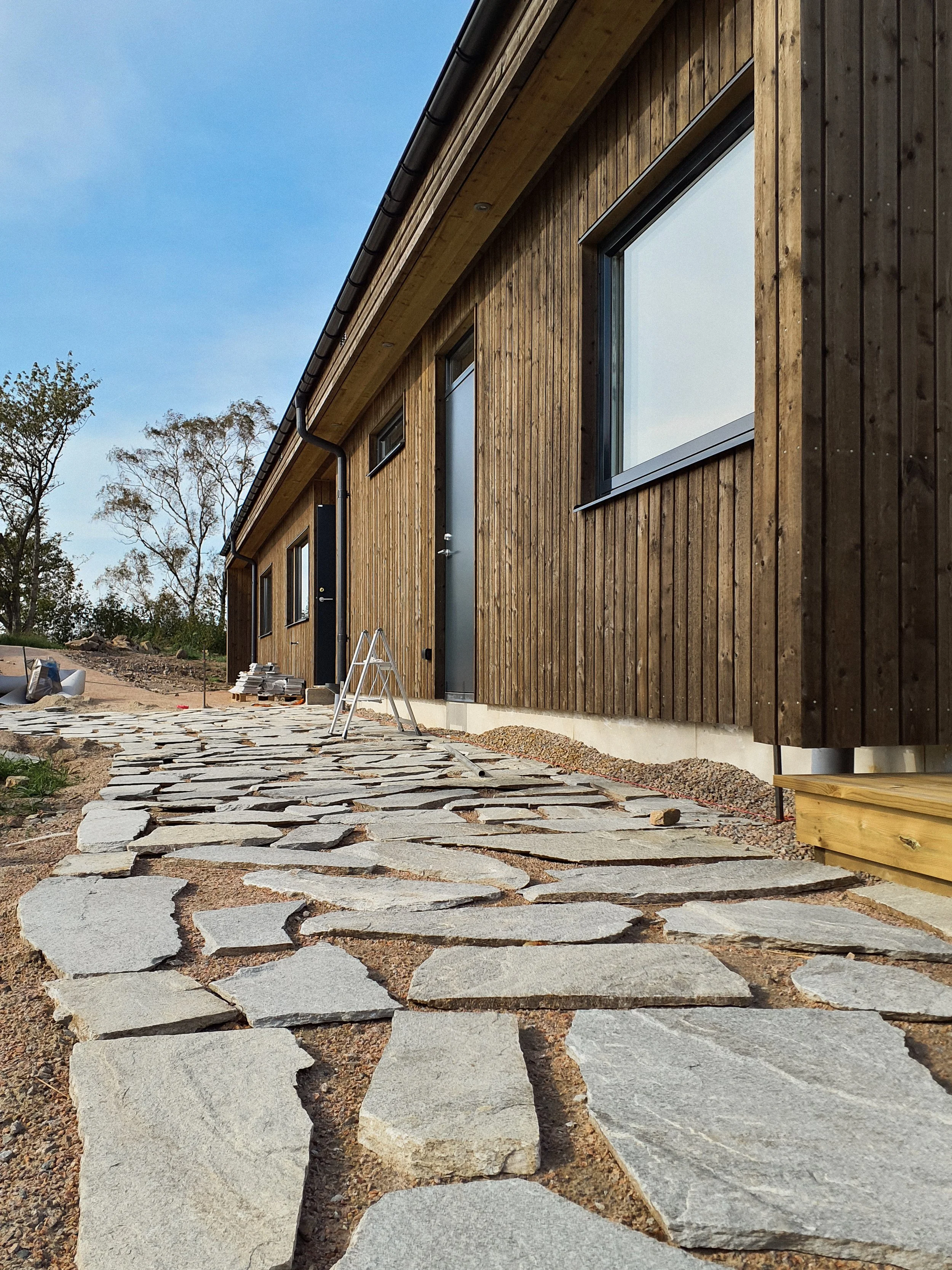 Nybyggt hus med träfasad och en stenlagd gångväg framför