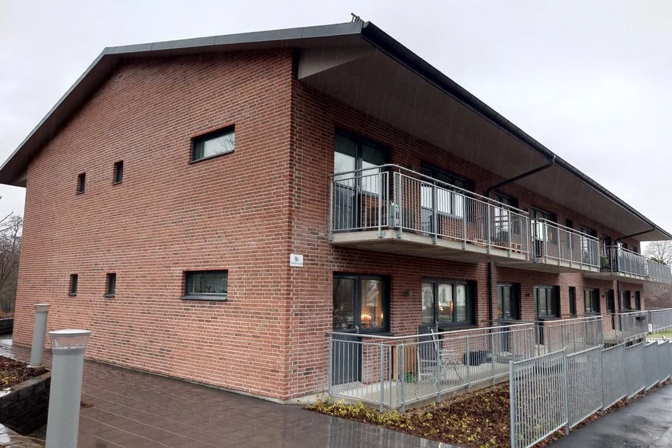 En modern flerfamiljsbostad med rödbrun tegelfasad och balkonger med metallräcken.