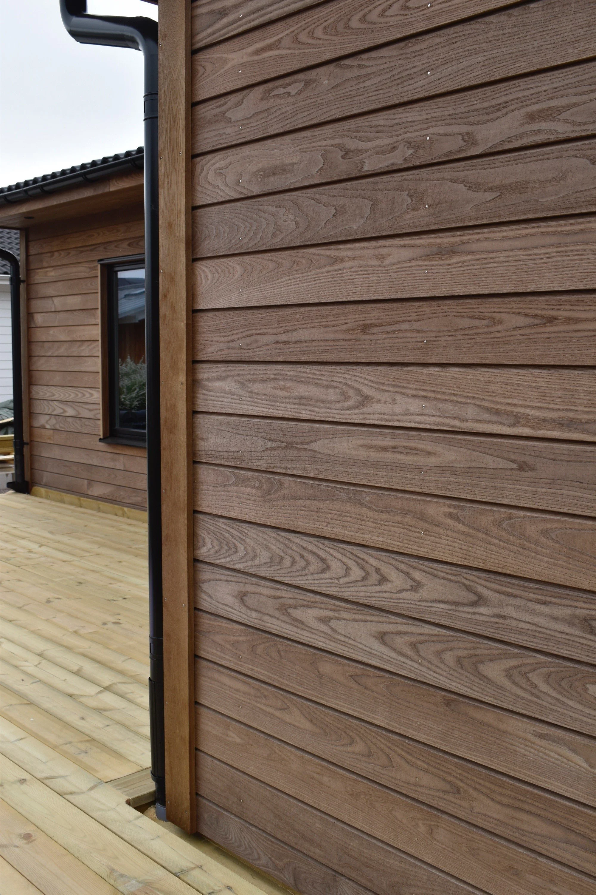 Närbild på en vägg av träpaneler på ett utomhushus, med fönster och trädäck.