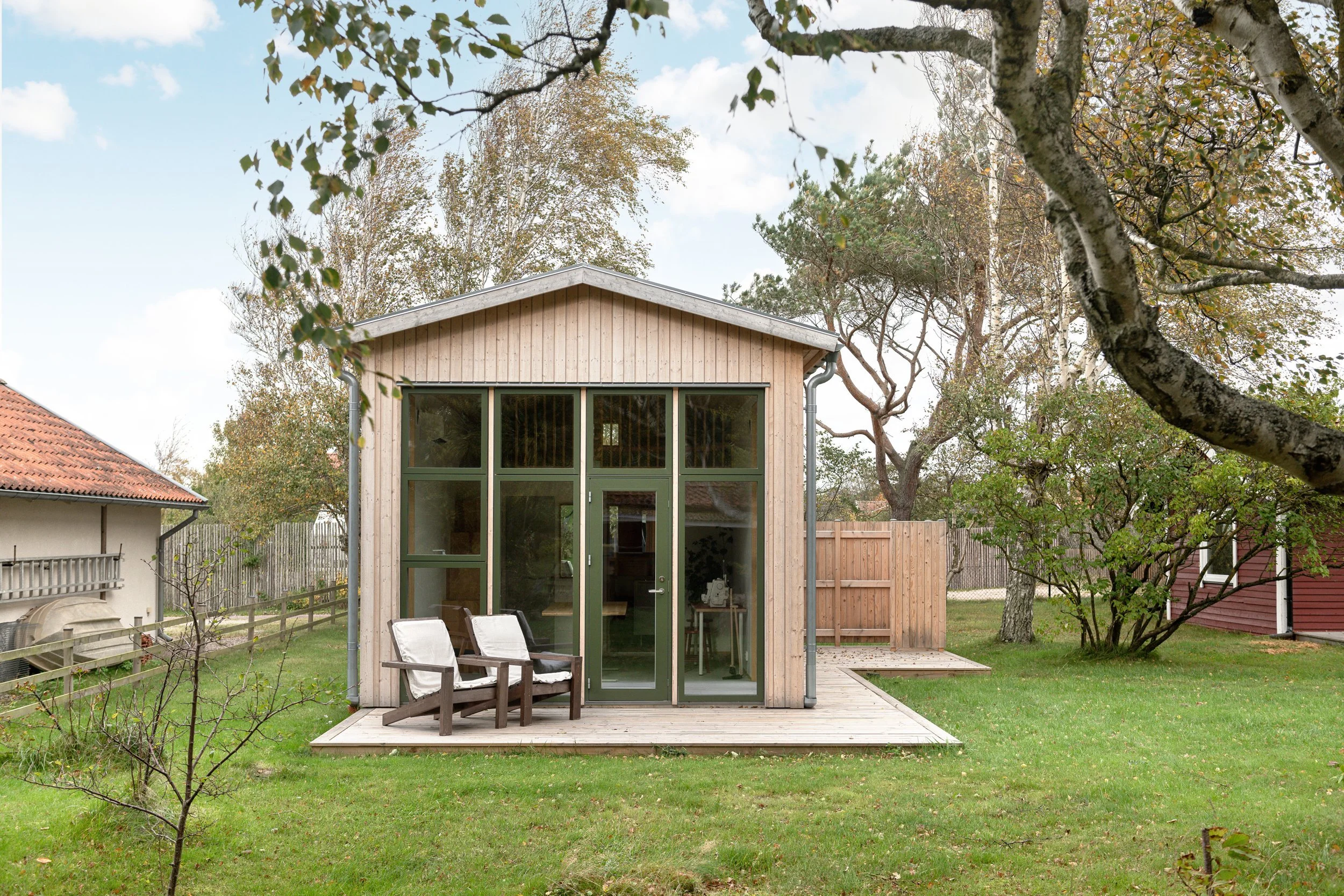 En liten modern stuga med glasdörrar och fönster, belägen i en trädgård med grönt gräs och träd runtom.