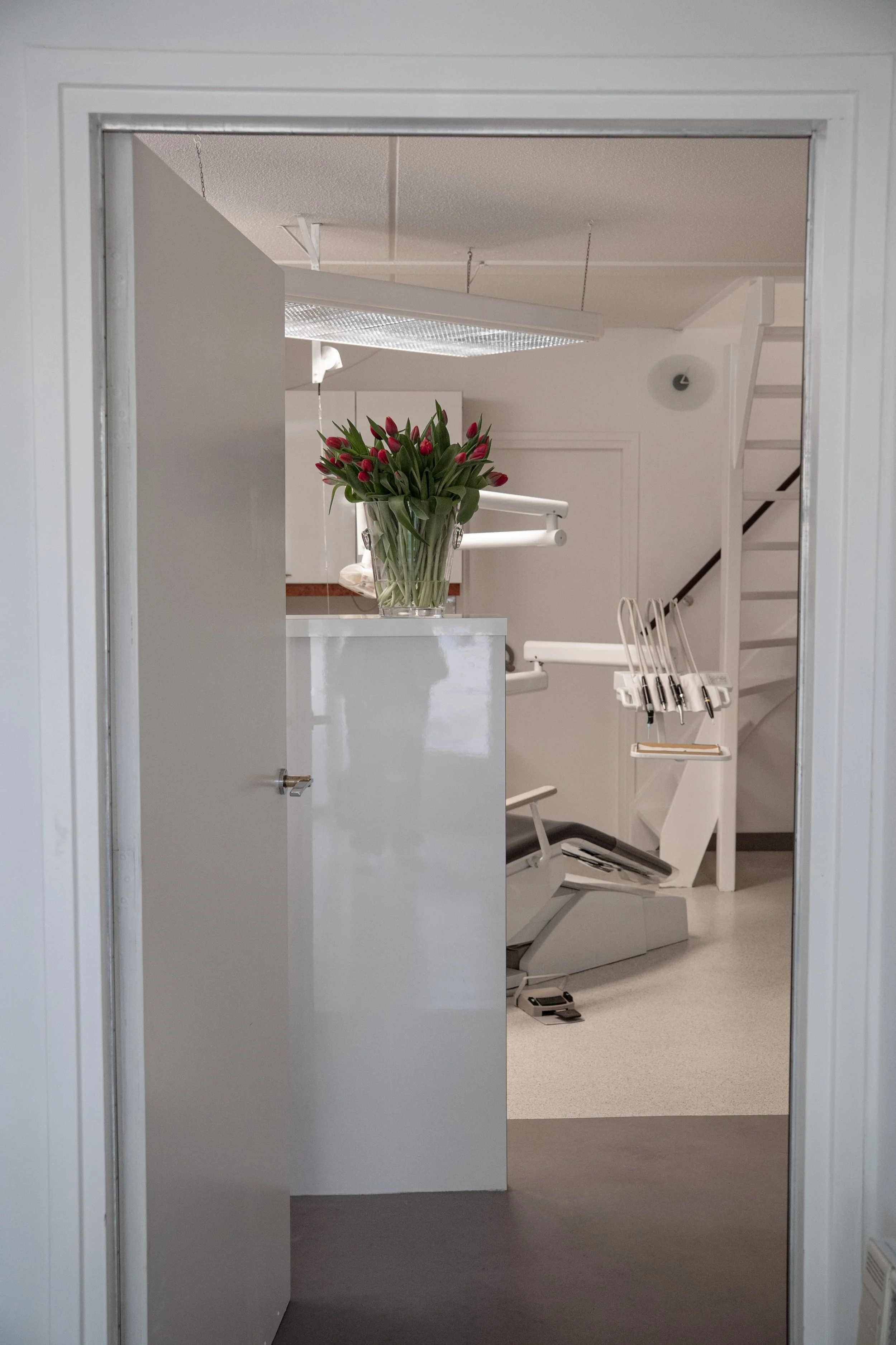 Een tandartspraktijk met een tandartsstoel, medische instrumenten en een vazen met rode tulpen. Wittewel. Tandenbleken.