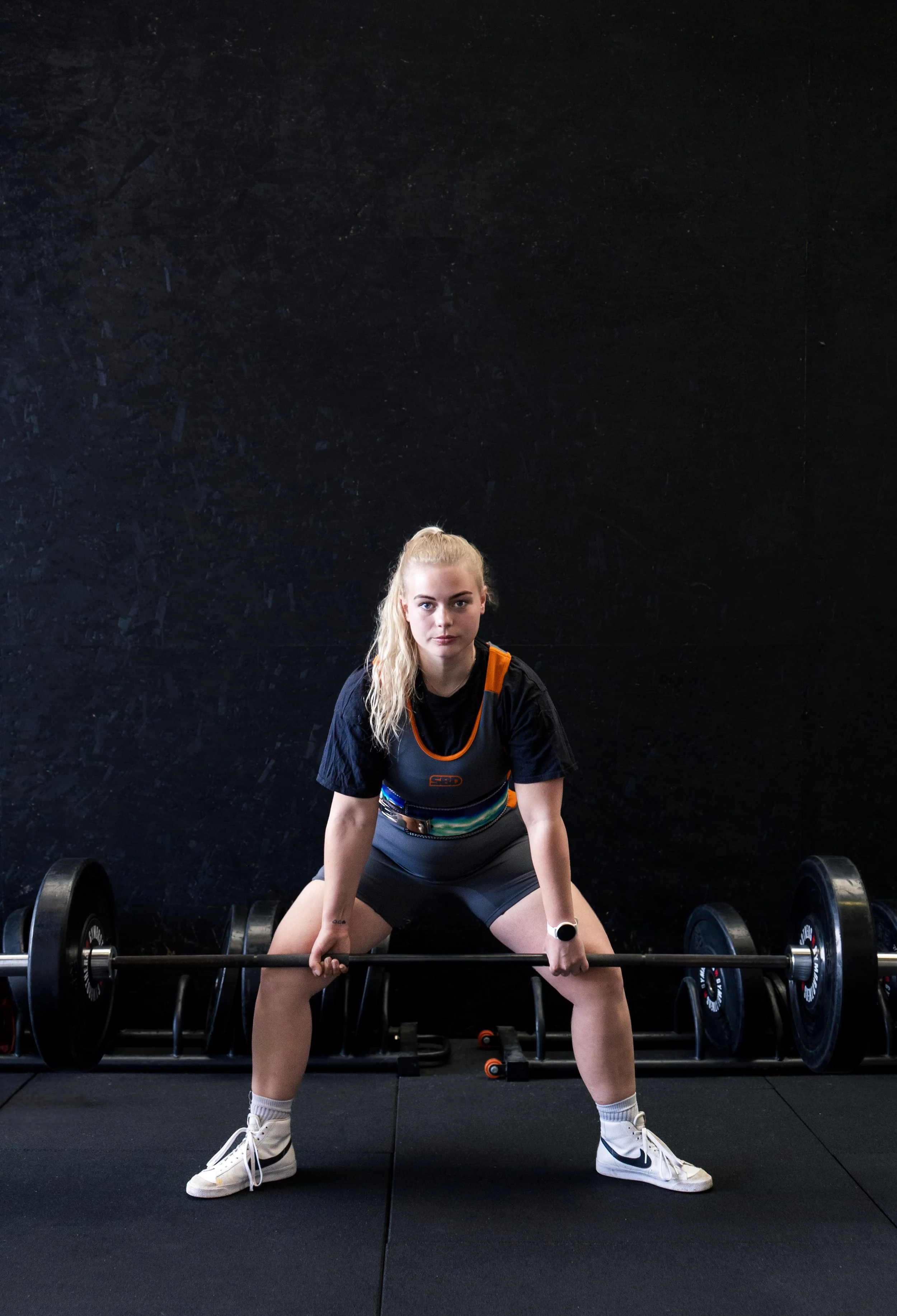 Vrouw tilt een halter in een sportschool met een zwarte muur op de achtergrond.