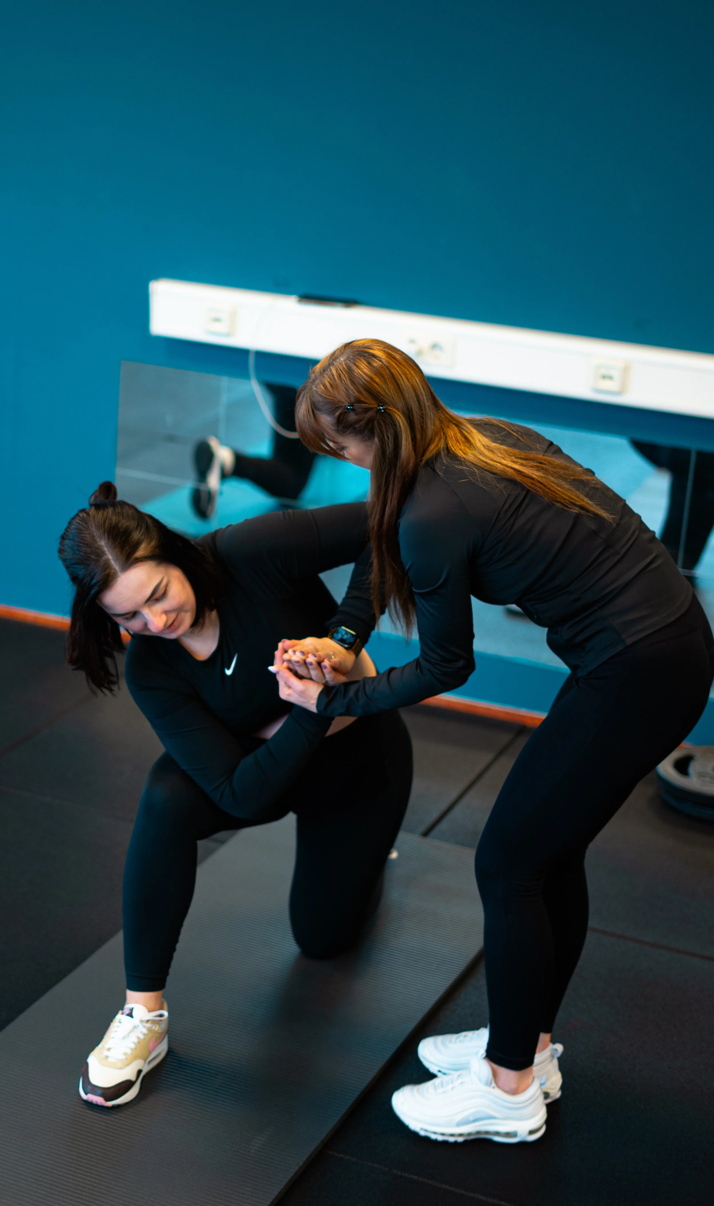 Een personal trainer helpt een vrouw bij een intake-oefening in een sportschool.