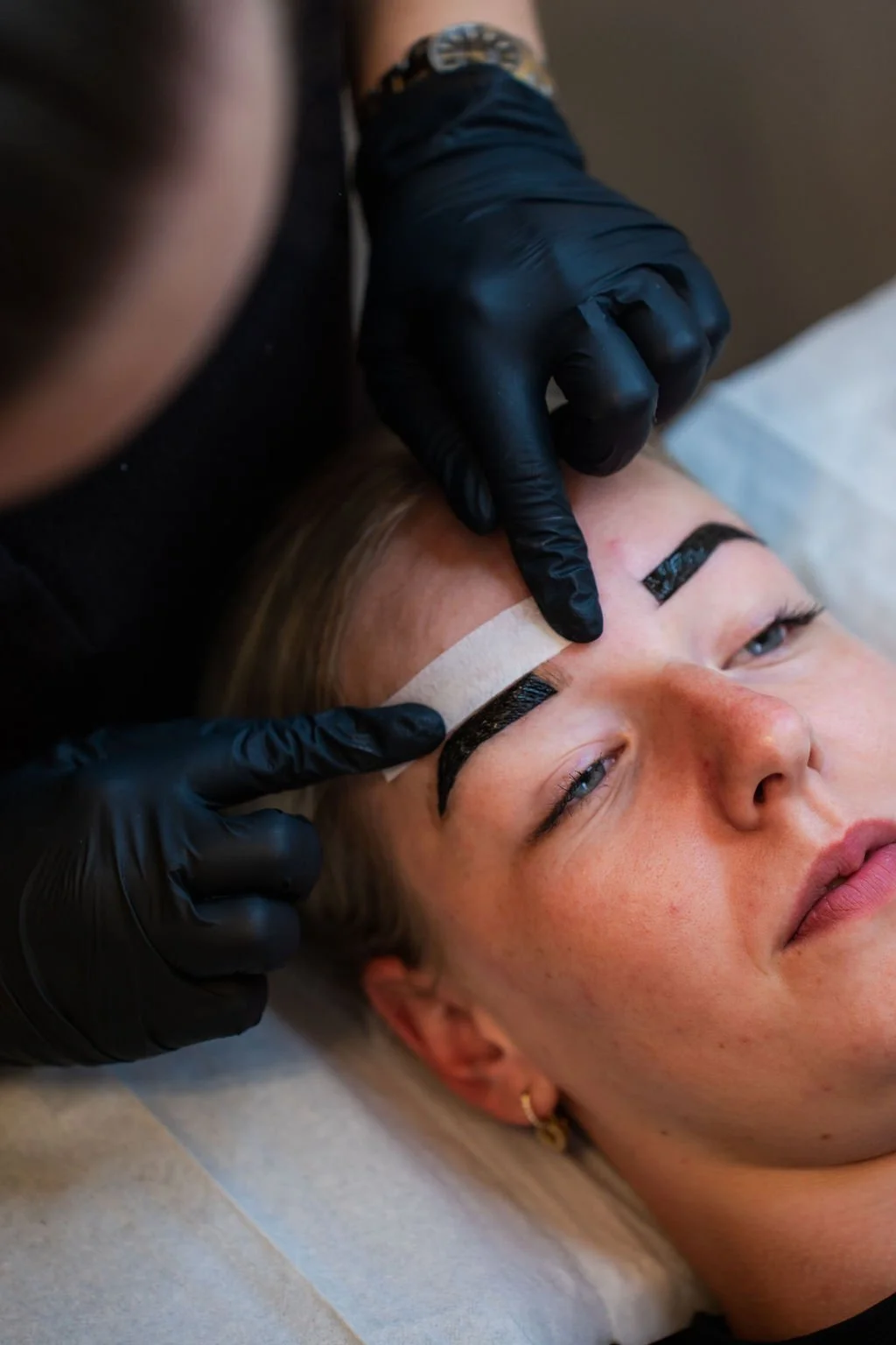 Vrouw krijgt een permanente eyeliner tatoeage op haar wenkbrauwen door een specialist met zwarte handschoenen. Beautysalon.