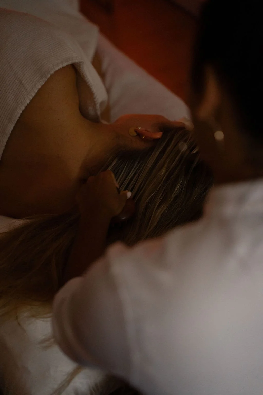 Close-up van een persoon die op een bed ligt, met een hoop kaarten in haar hand en een oorbel met een ronde gouden knop. Japanse headspa massage. Selfcare moment