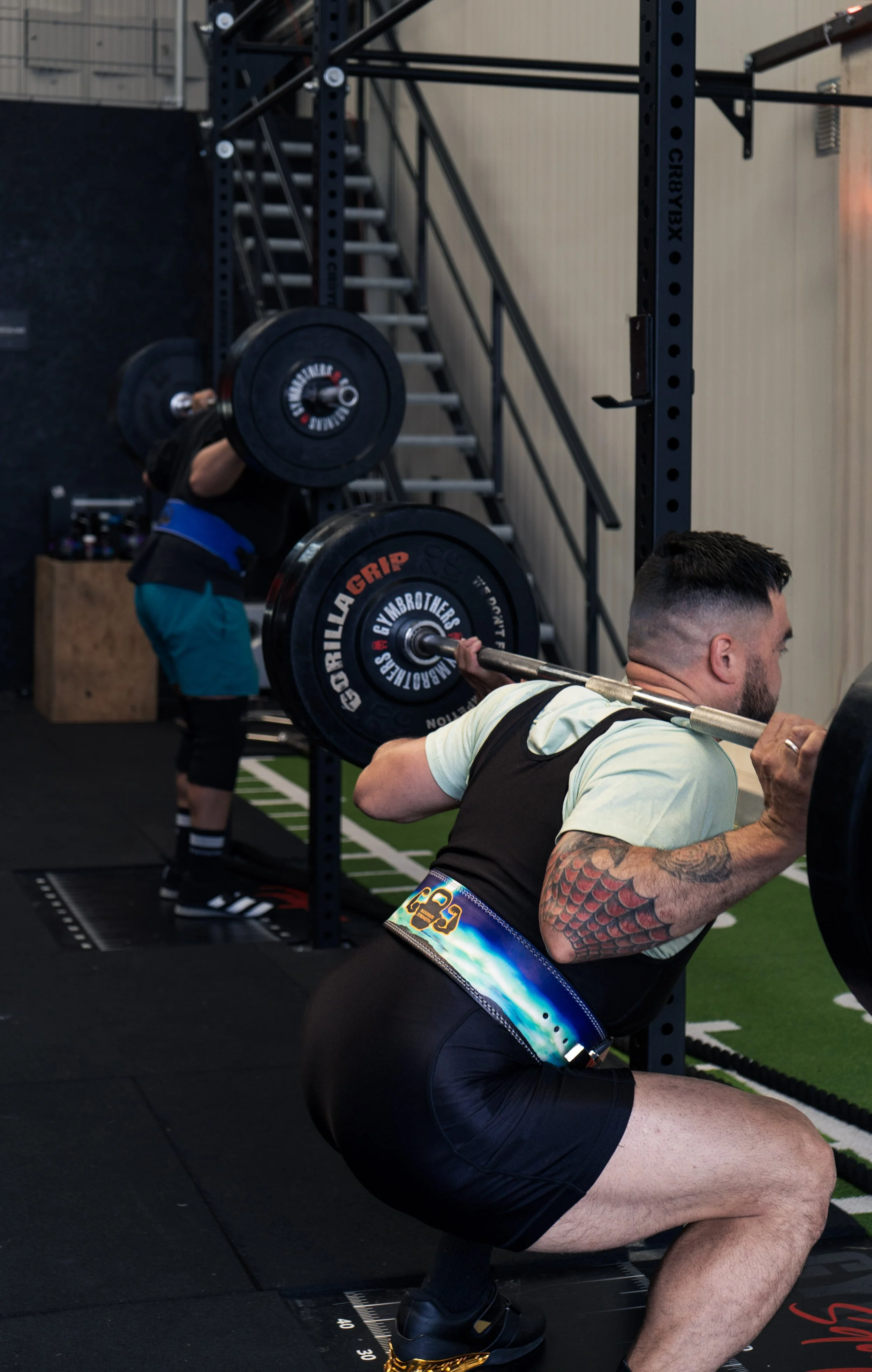 Twee mannen doen squats met barbells in een sportschool