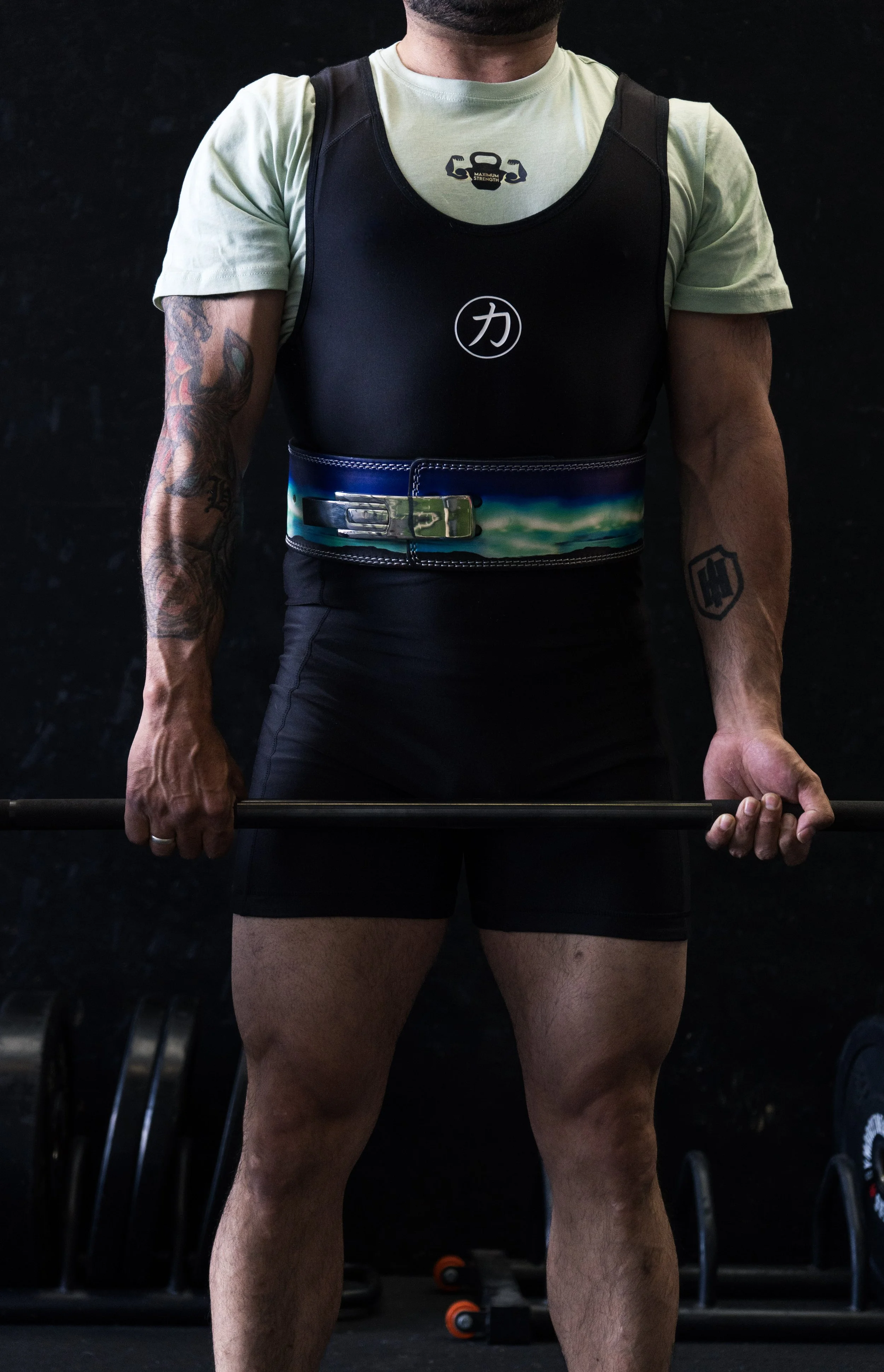 Men die krachttraining doet, met een gewichthefriem en een gewichtsstok, in een sportschool, met tattoos op zijn armen.