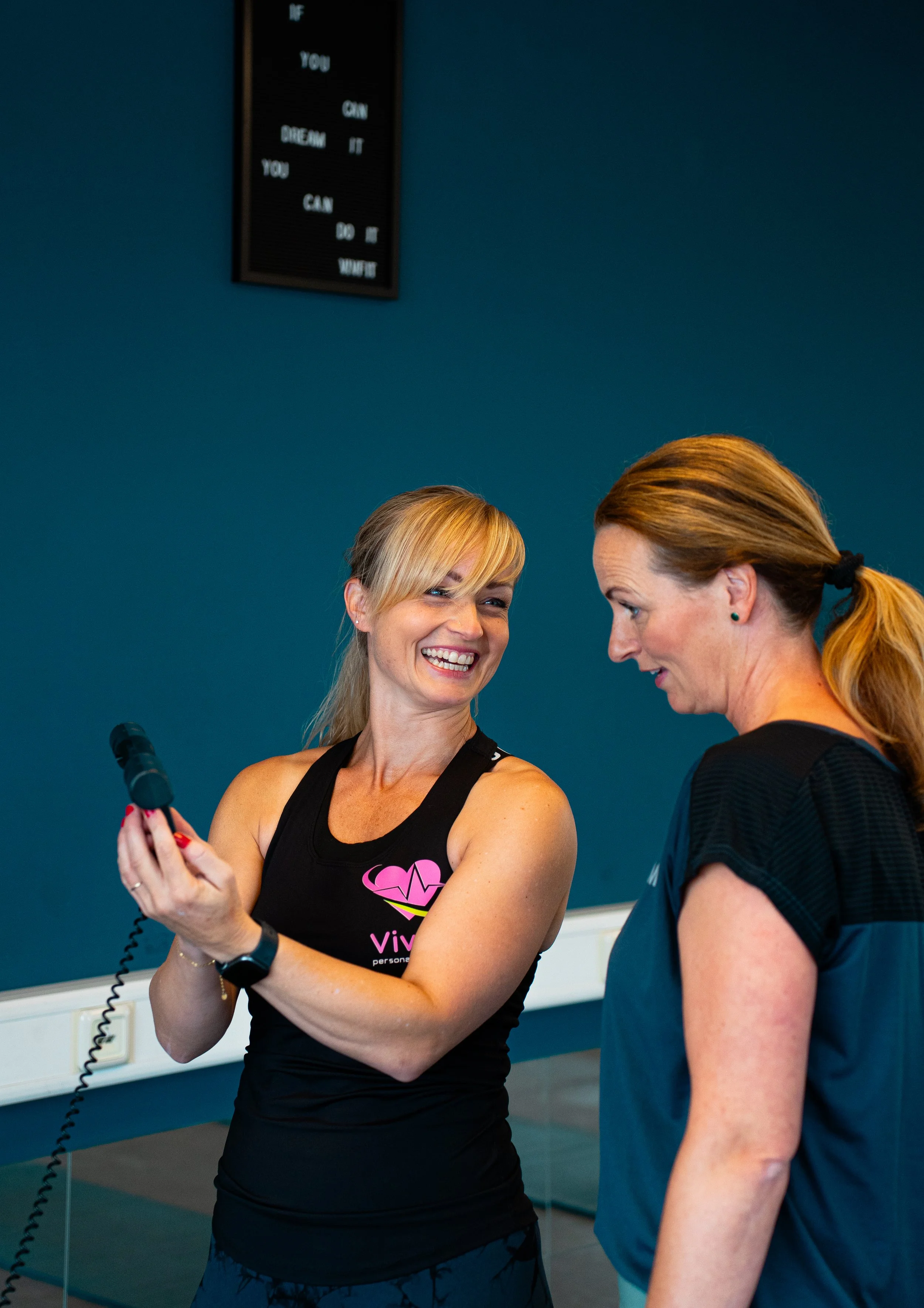 Tweede vrouw met lang haar in een paardenstaart praat met een lachende vriendin tijdens een sportles in de sportschool.