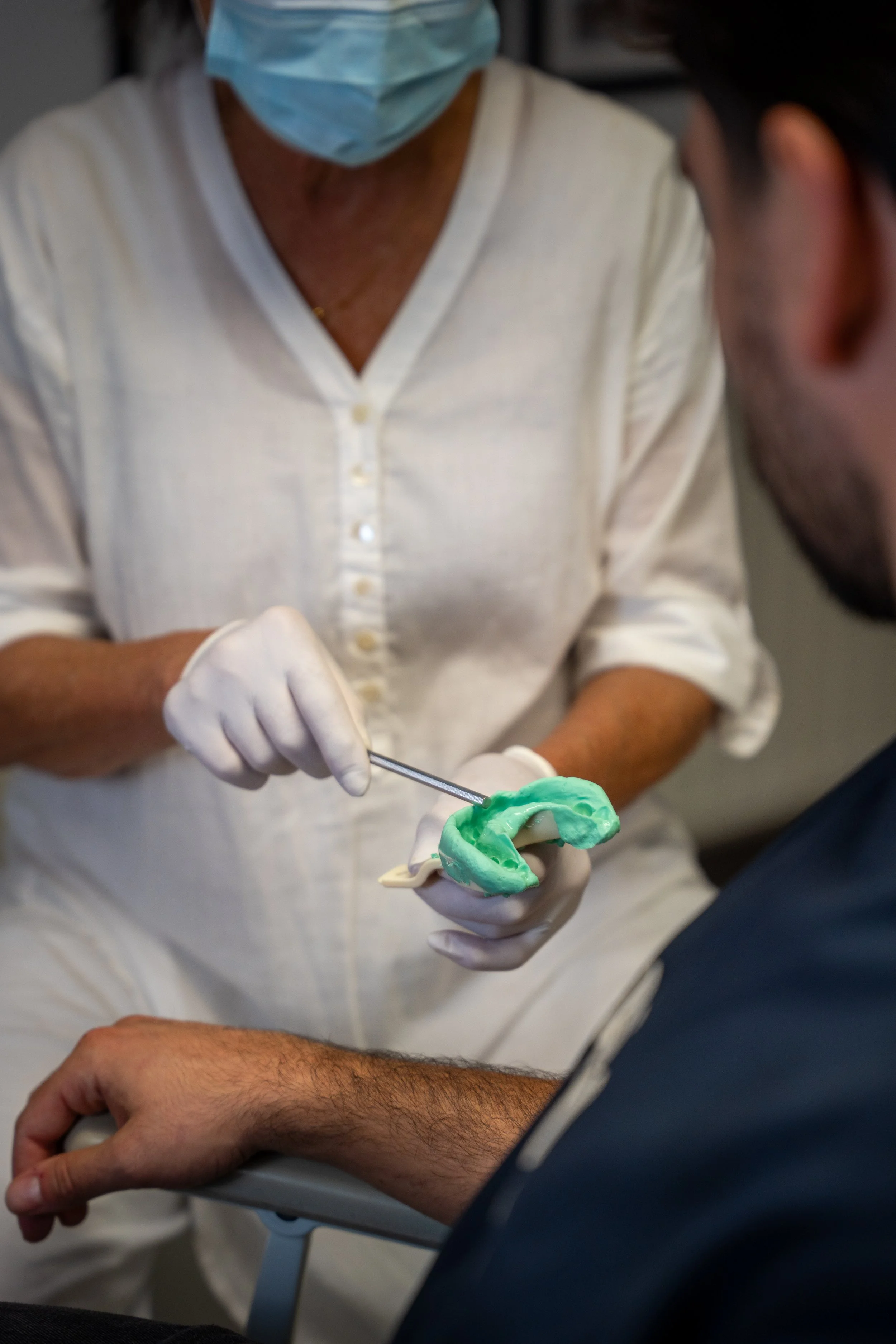 Tandarts die een stuk voorprothese of beugel toont aan een patiënt in een tandartspraktijk. Wittewel. Tandenbleken.