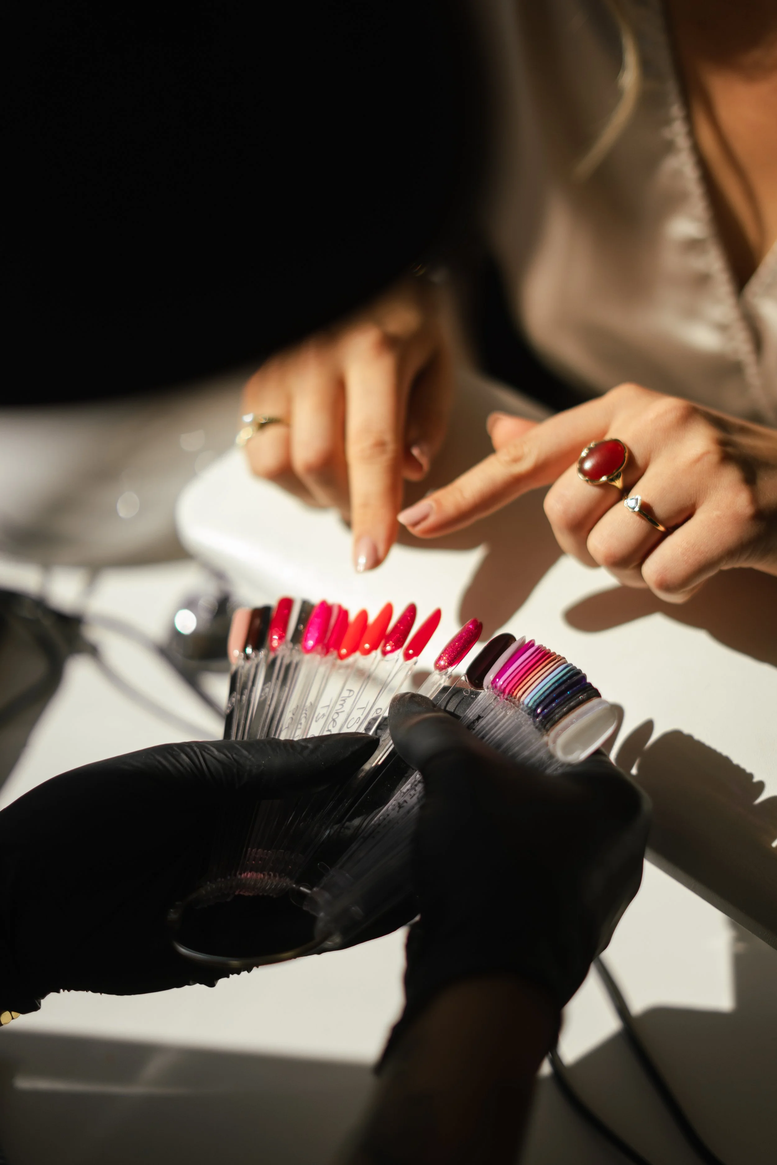 Personen kiezen nagellak uit een kleurenwaaier met behulp van een persoon met zwarte handschoenen.