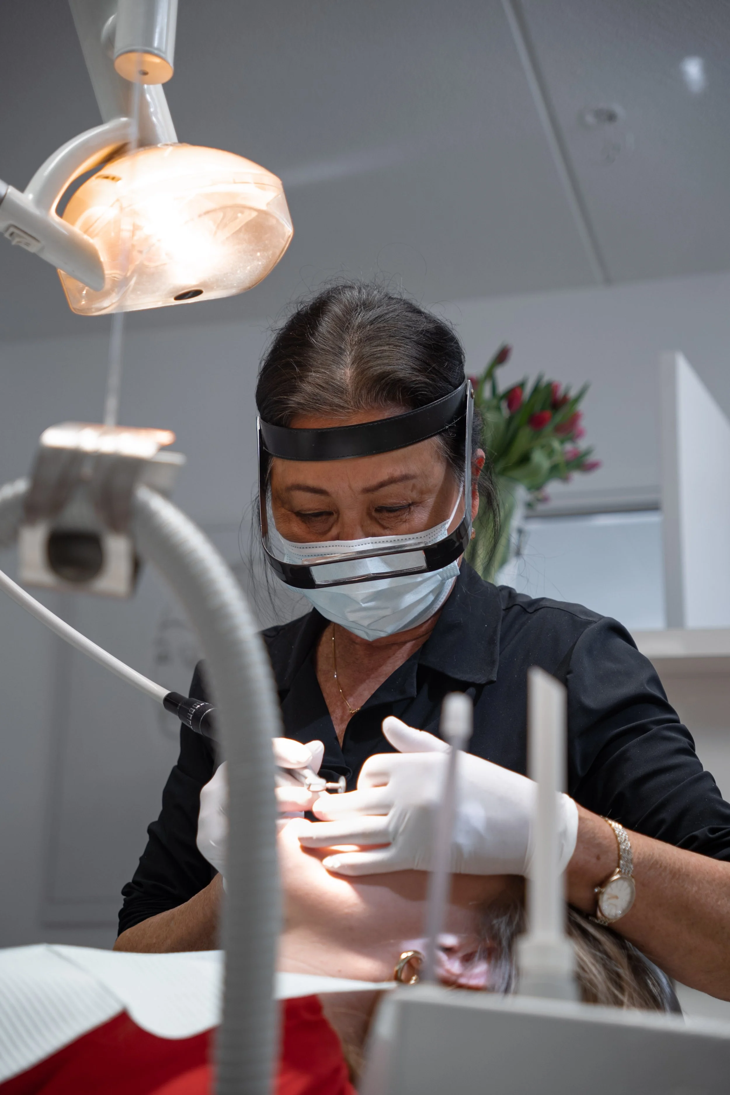 Een vrouwelijke tandarts is bezig met een tandheelkundige behandeling, ze draagt een gezichtsbeschermende bril, mondkapje, witte handschoenen en gebruikt een instrument tijdens de behandeling. Wittewel. Tandenbleken.