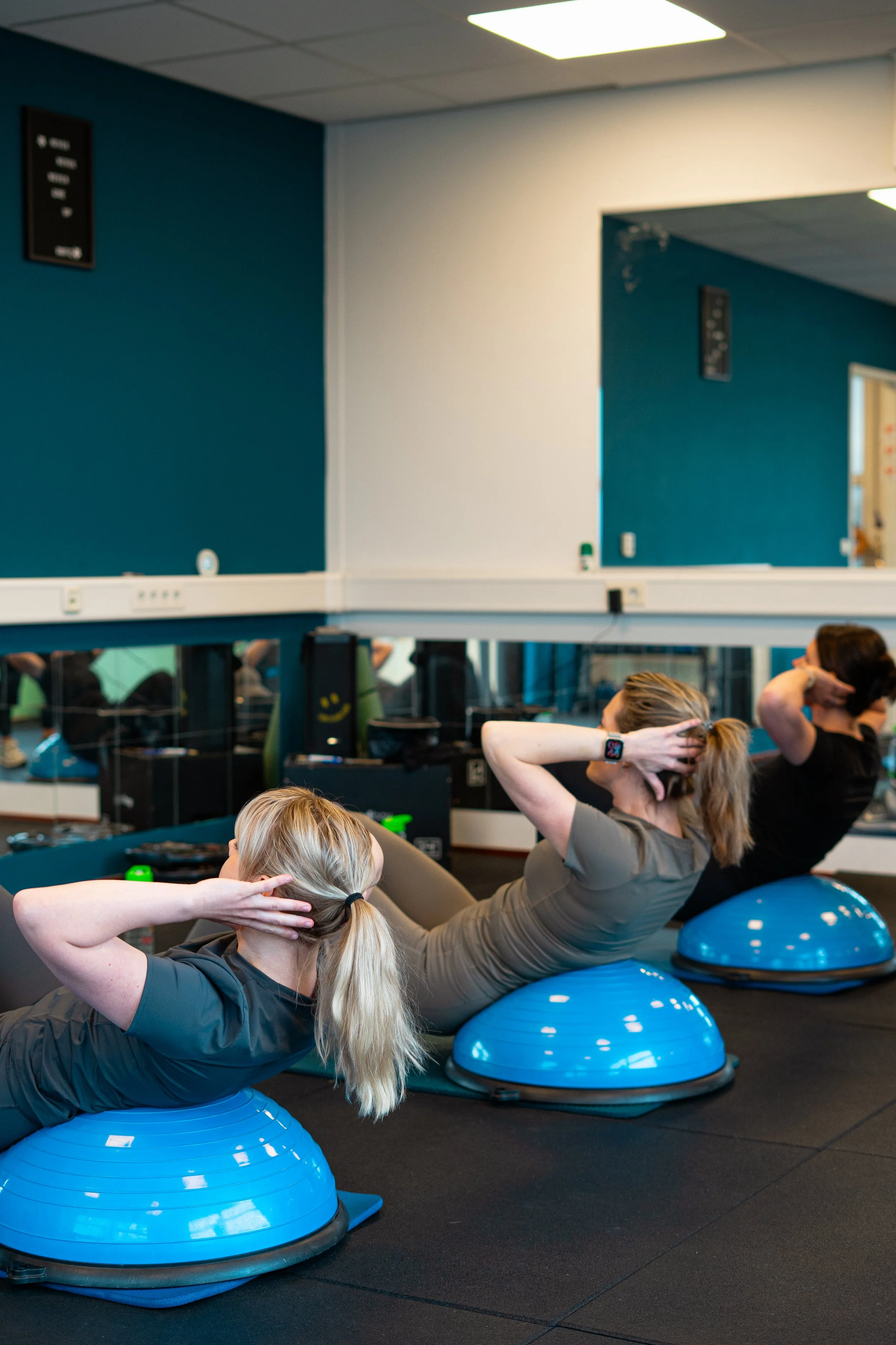 Drie vrouwen doen buikspieroefeningen met behulp van BOSU balancing balls in een fitnessruimte.