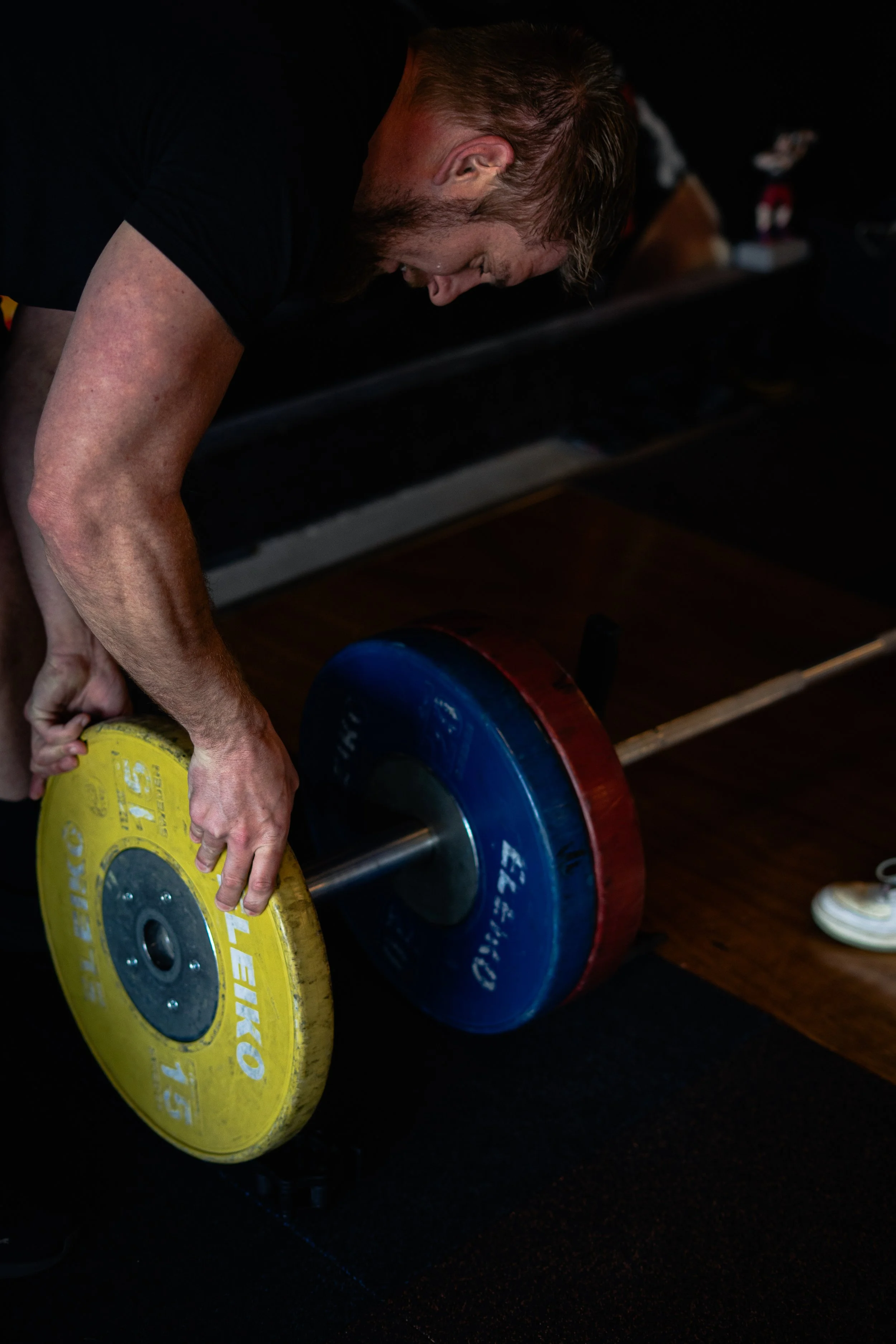Man tiltte een halter met gekleurde gewichtschijven in een fitnessruimte. Sportschool Emmen. Krachttraining. Deadlift