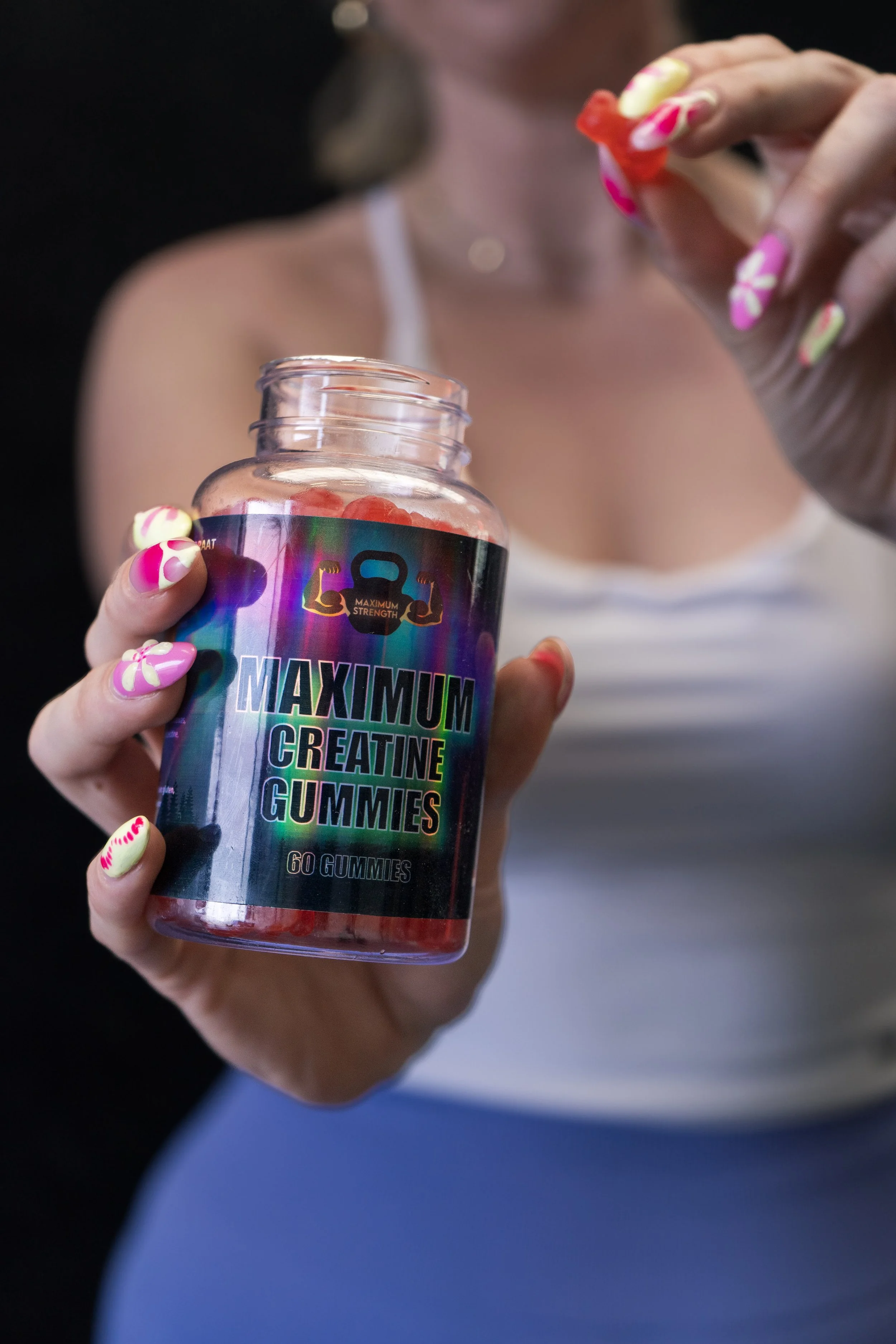 Een vrouw houdt een pot met maximale creatine-gummies en pakt er een uit.