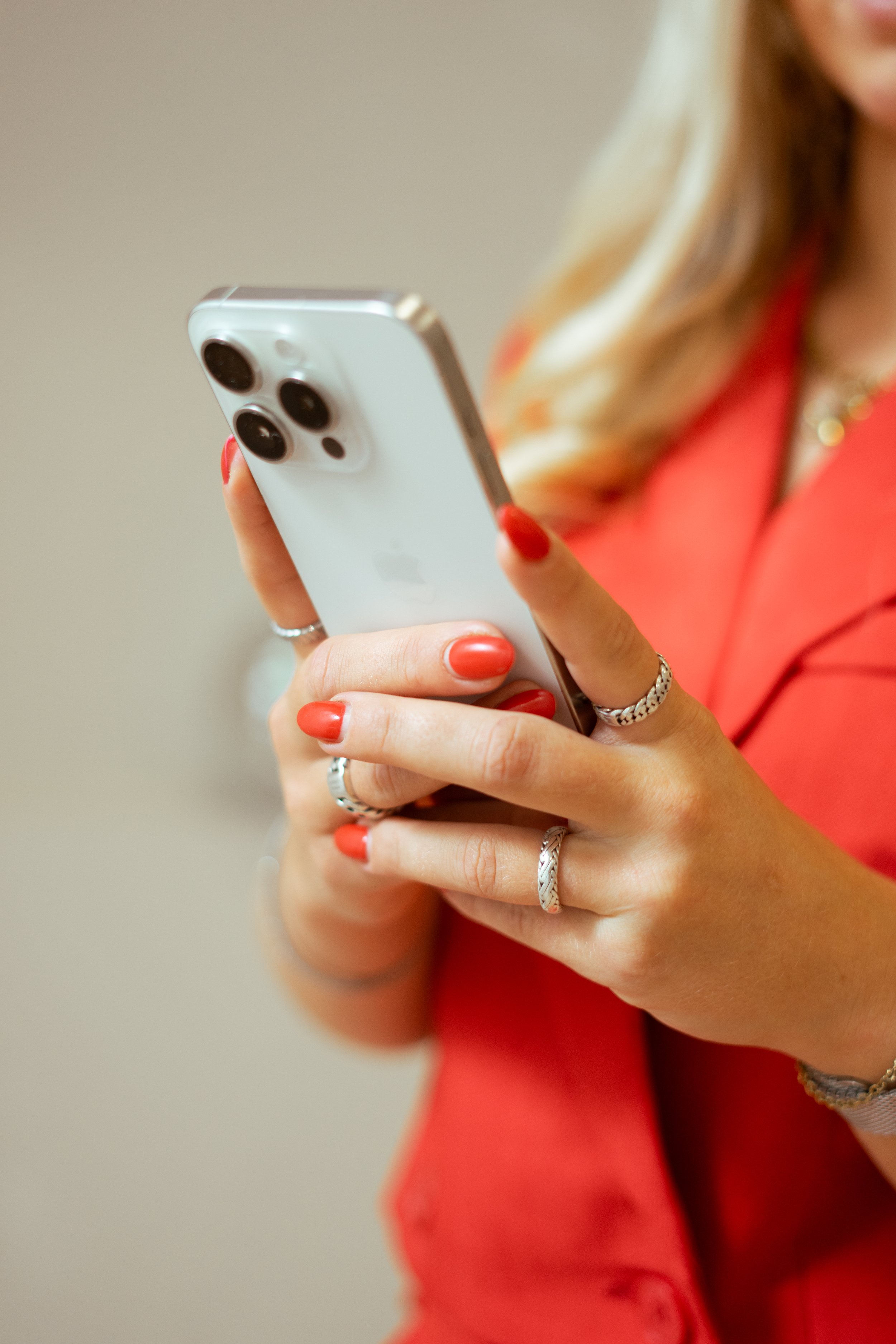 Een vrouw met rood/oranje lak op haar nagels houdt een iPhone vast.