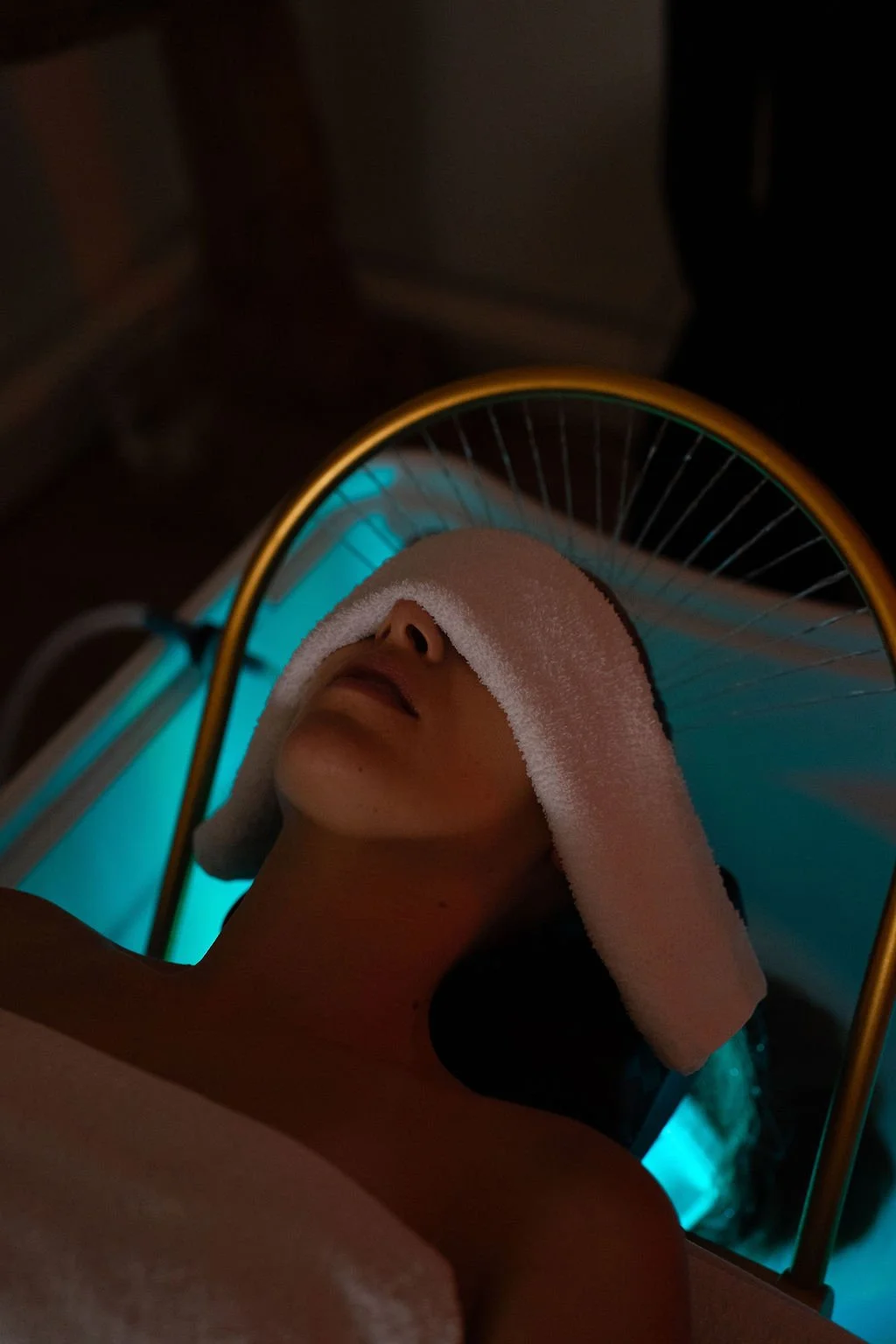 Persoon met een handdoek op haar hoofd ligt onder een warmtestraler in een hammam of wellnesscentrum. Japanse headspa massage. Selfcare moment