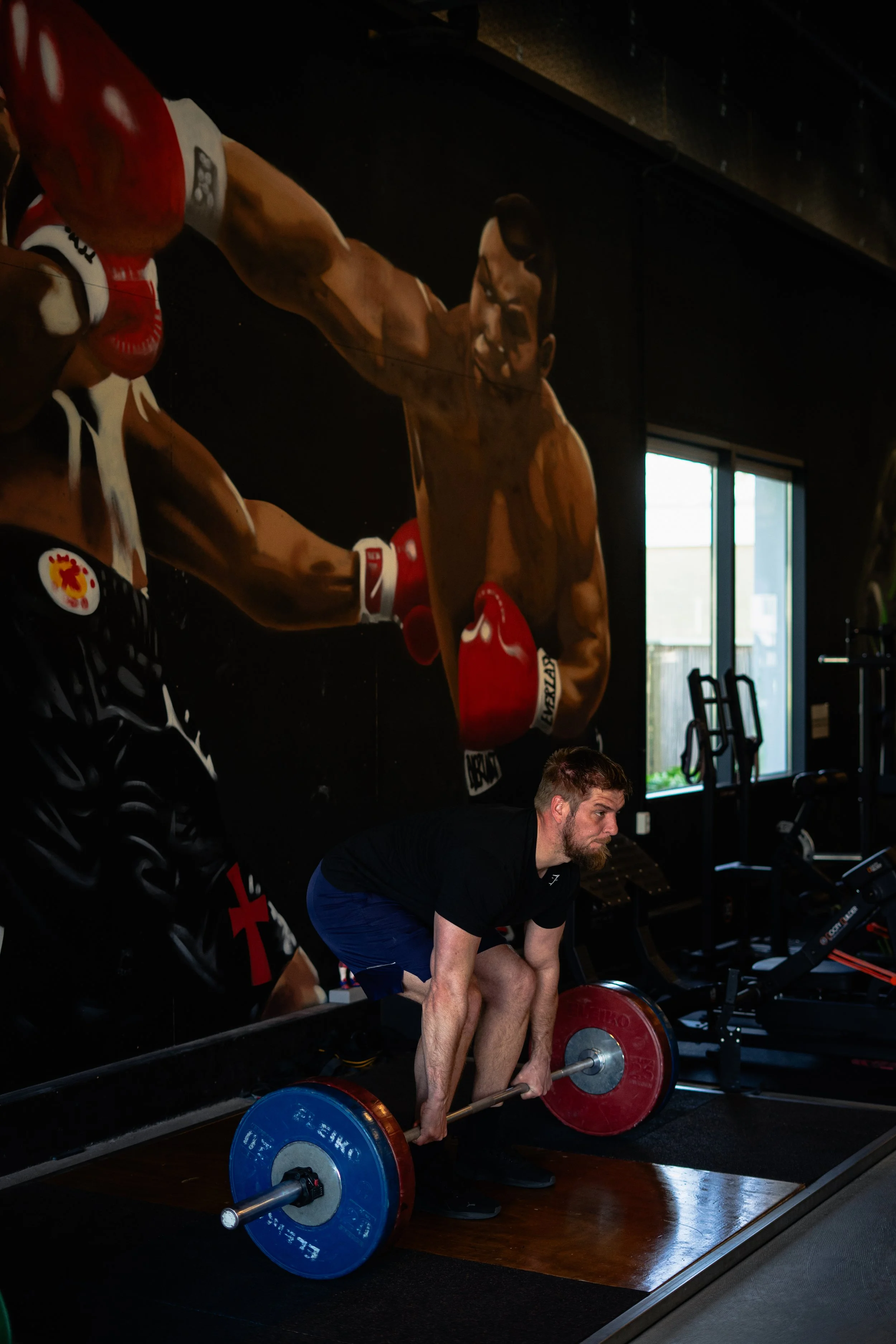 Man in zwart shirt en blauwe shorts doet deadlift met zware barbell in een sportschool. Emmen. Krachttraining.