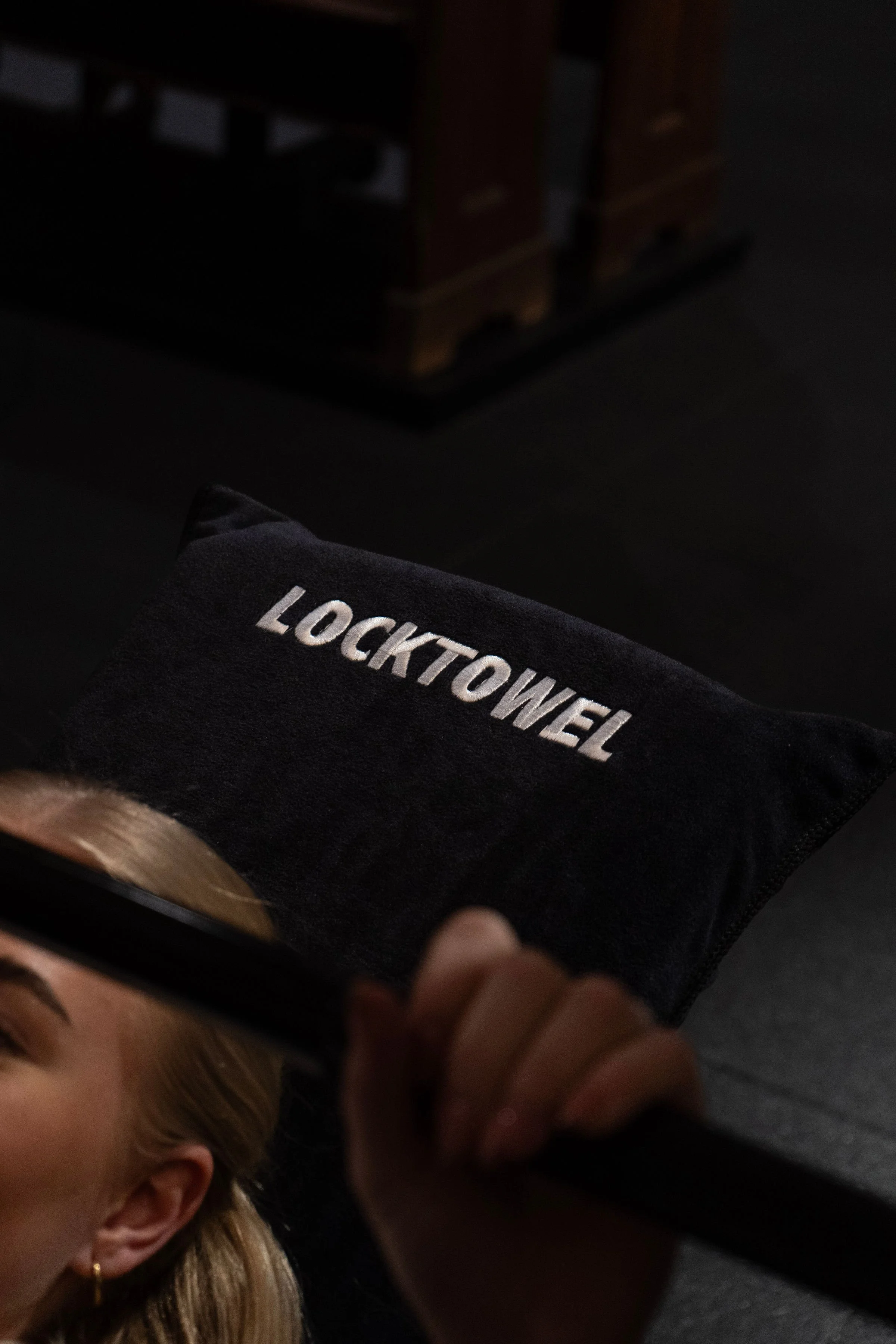 Persoon die een black doekje vasthoudt met de tekst 'LOCKTOWEL' erop, terwijl een deel van haar gezicht en haar hand zichtbaar is.