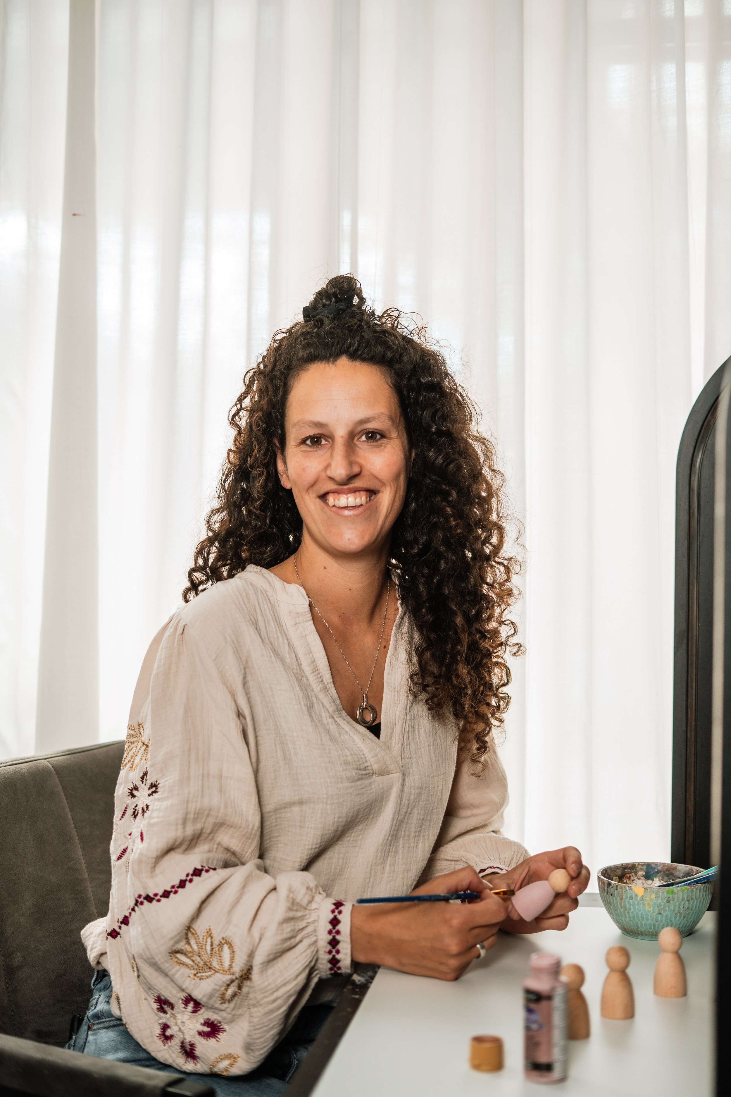 Vrouw met krullend haar die schilderen of tekenen, zittend aan een tafel met een kom en kleine houten poppetjes