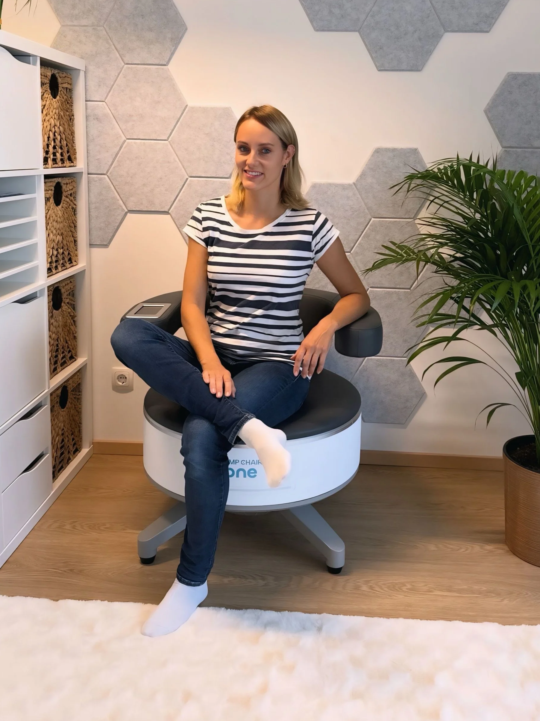 Junge Frau sitzt entspannt auf dem EMP Chair Pro One in einem modern eingerichteten Raum, umgeben von Dekorationen wie Pflanzen und hexagonalen Wandfliesen.