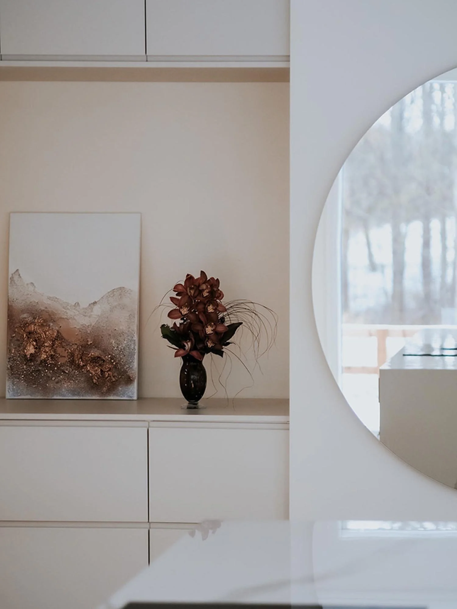Sisustustyylinen sisäkuva, jossa valkoinen kaapisto, seinälle ripustettu taide, maljakko lukunaan ja ikkunasta näkyvät ulkovalot.