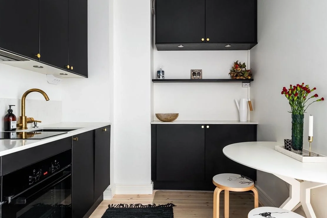 Tyylikäs keittiö, jossa mustat kaapit ja valkoinen työpöytä, koriste-esineitä ja kukkavaasi.