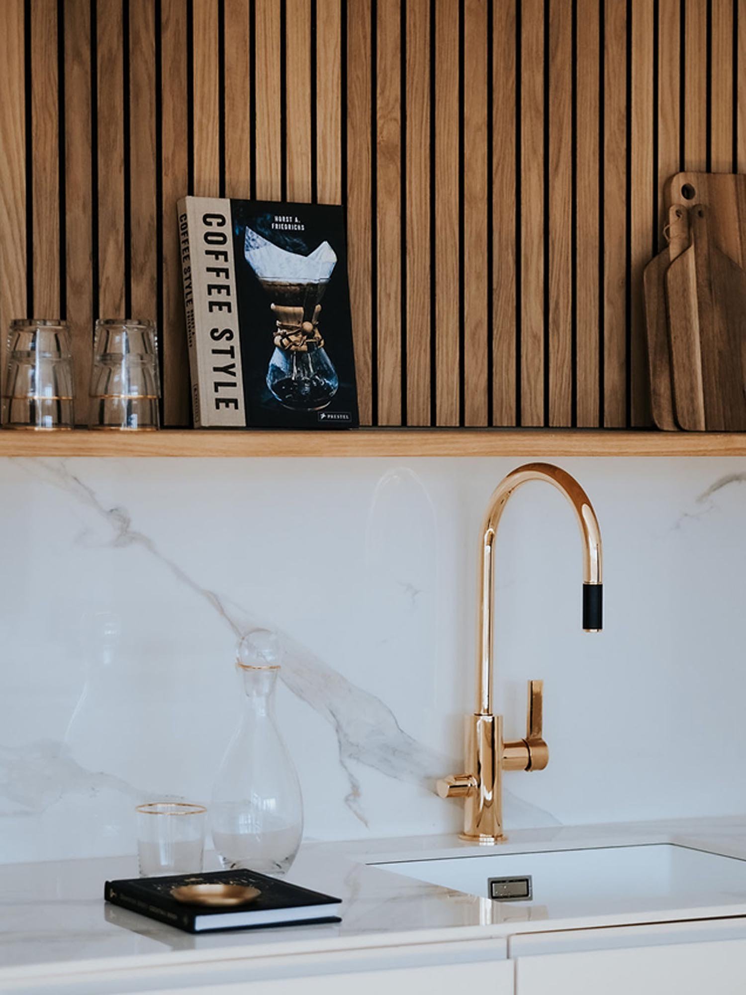 Korkeakiiltoinen messinkinen hana keittiössä. Taustalla puupaneeli ja kaksi leikkuulautaa.