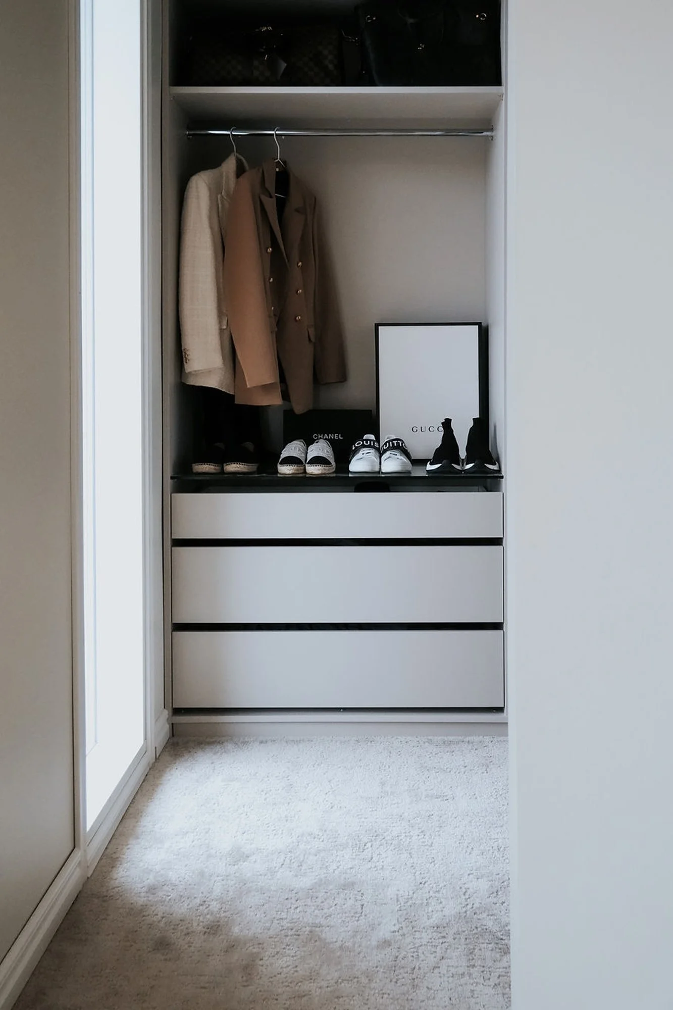 Vaalea ja minimalistinen vaatekaappi, jossa avoin vaatetanko takeille, hylly käsilaukuille, laatikosto sekä siististi asetellut kengät. Skandinaavinen ja hillitty sisustus.