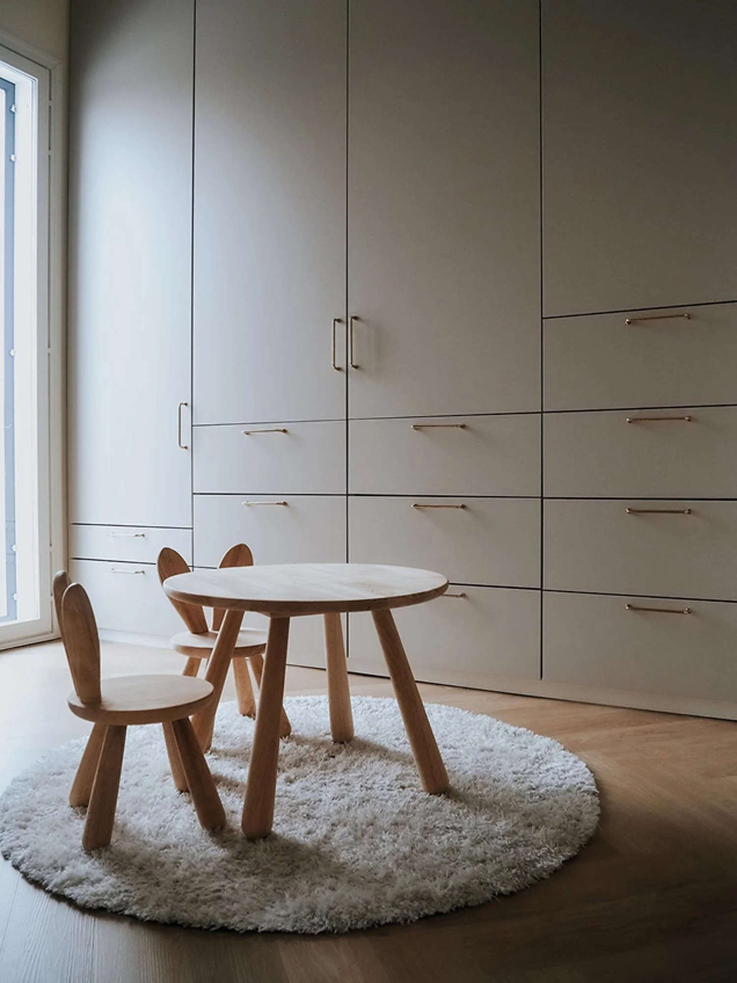 Lastenhuone, jossa taustalla iso vaalea kaapisto, lattialla pyöreä matto ja pieni pöytä sekä kaksi pientä tuolia.