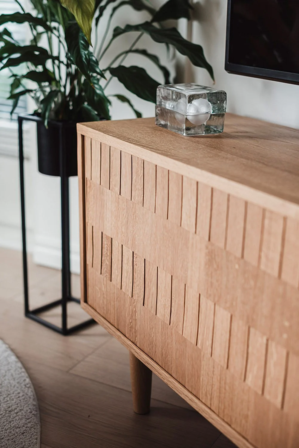 Punen senkki tv:n alla ja näyttävä viherkasvi korkeassa ruukussa.