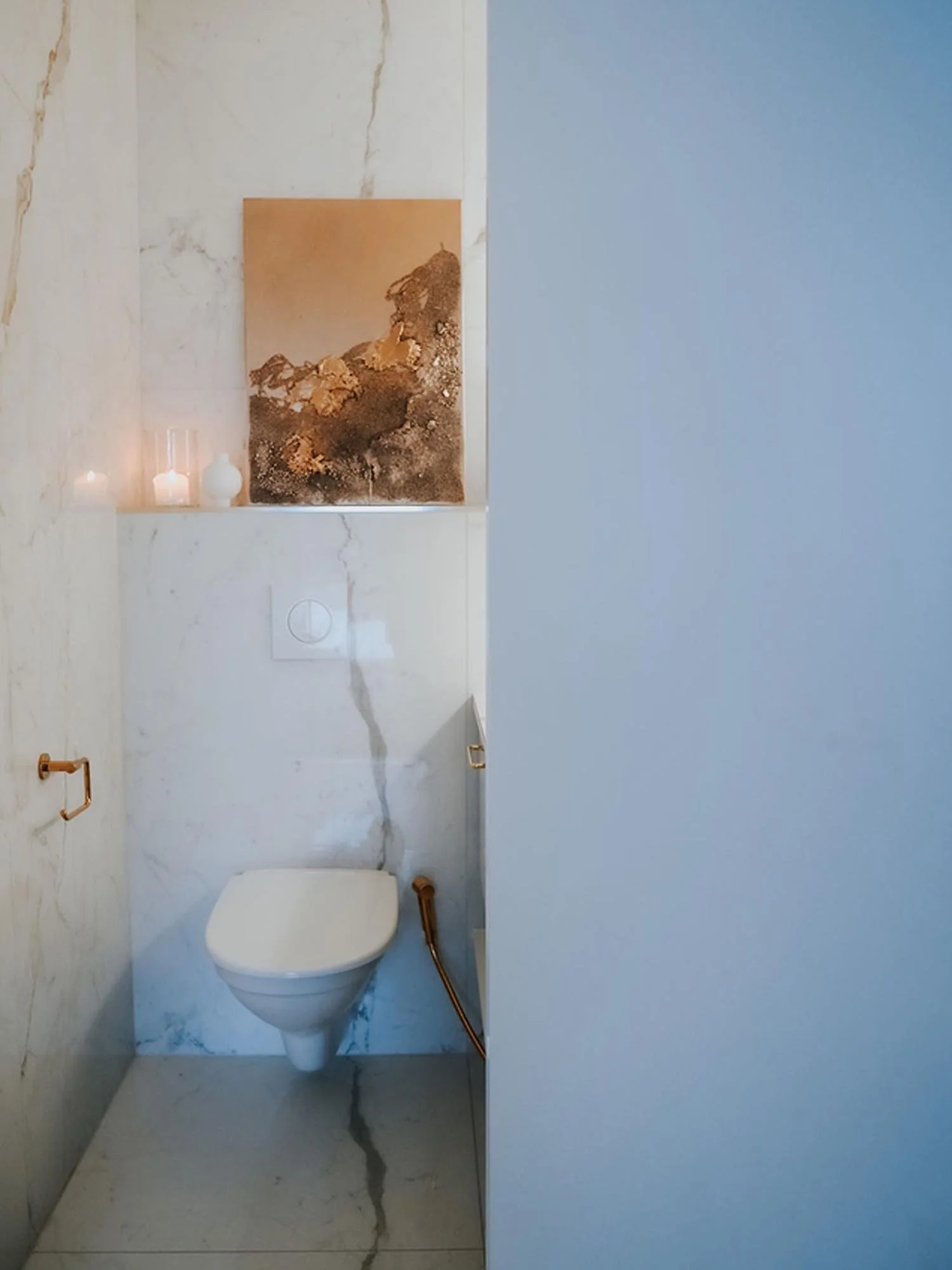 Näkymä wc-tilaan, jossa seinässä oleva wc ja yläpuolella taidetta.