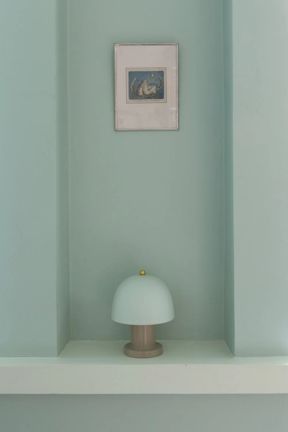 Kuvassa on vihreä seinä, jossa on kehystetty taideteos, ja sen alla pieni pöytävalaisin.