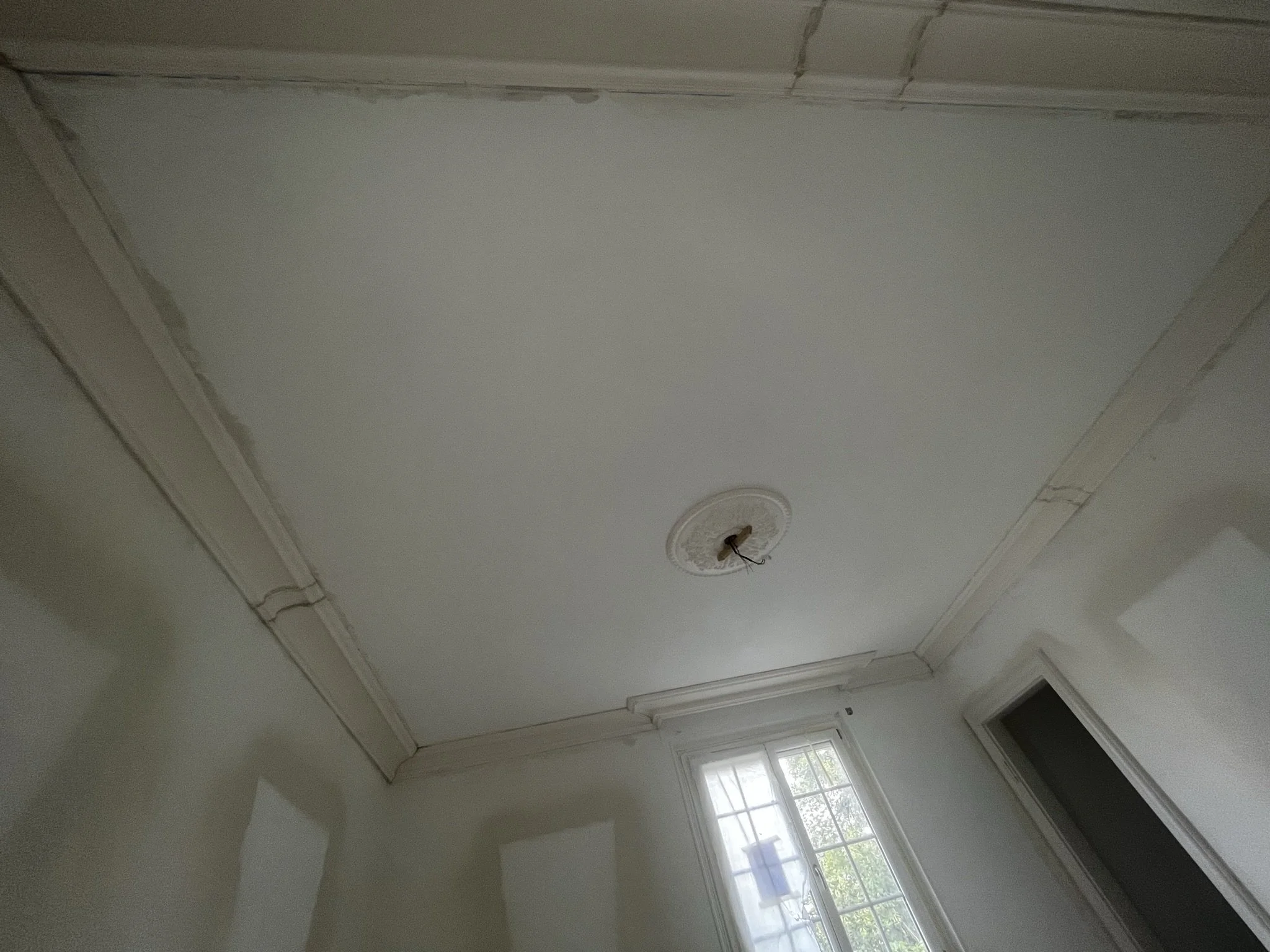 Plafond en cours de rénovation dans une pièce, avec un mur blanc et une fenêtre à la lumière naturelle.