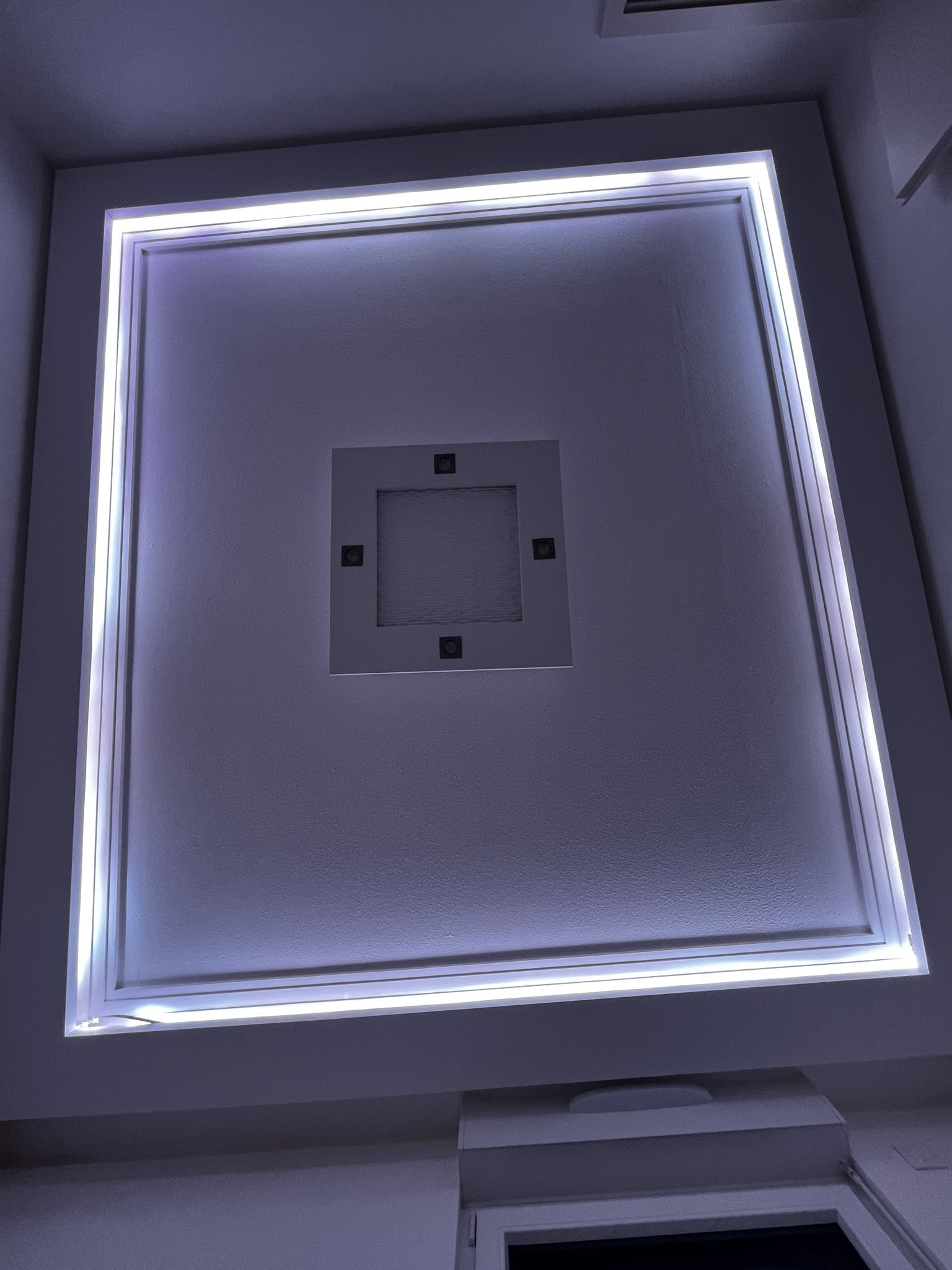 Plafond sur mesure en staff avec éclairage LED blanc autour de ses bords et un plafonnier en plâtre au centre